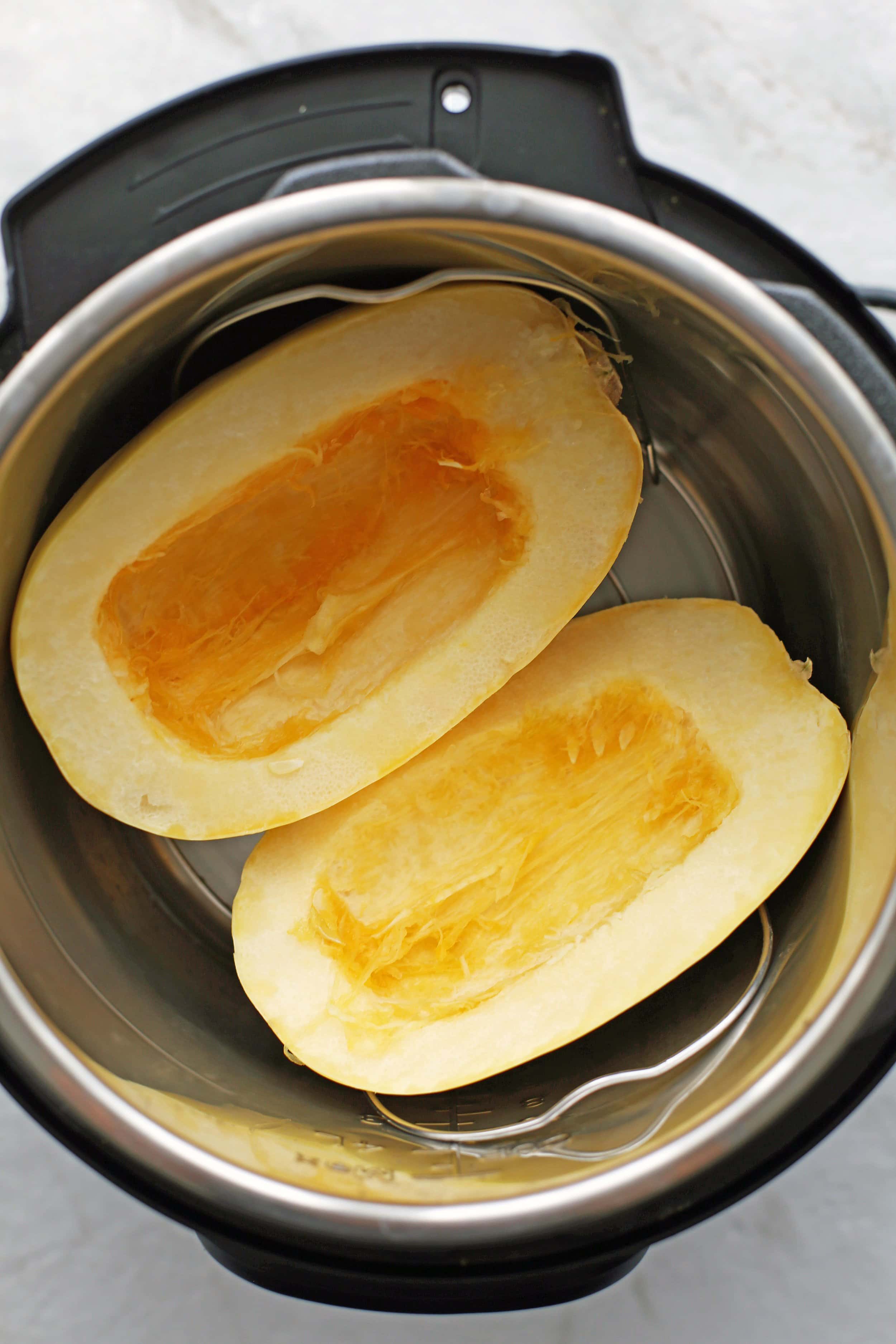 A halved and seeded spaghetti squash cut side up on a metal trivet in the Instant Pot.