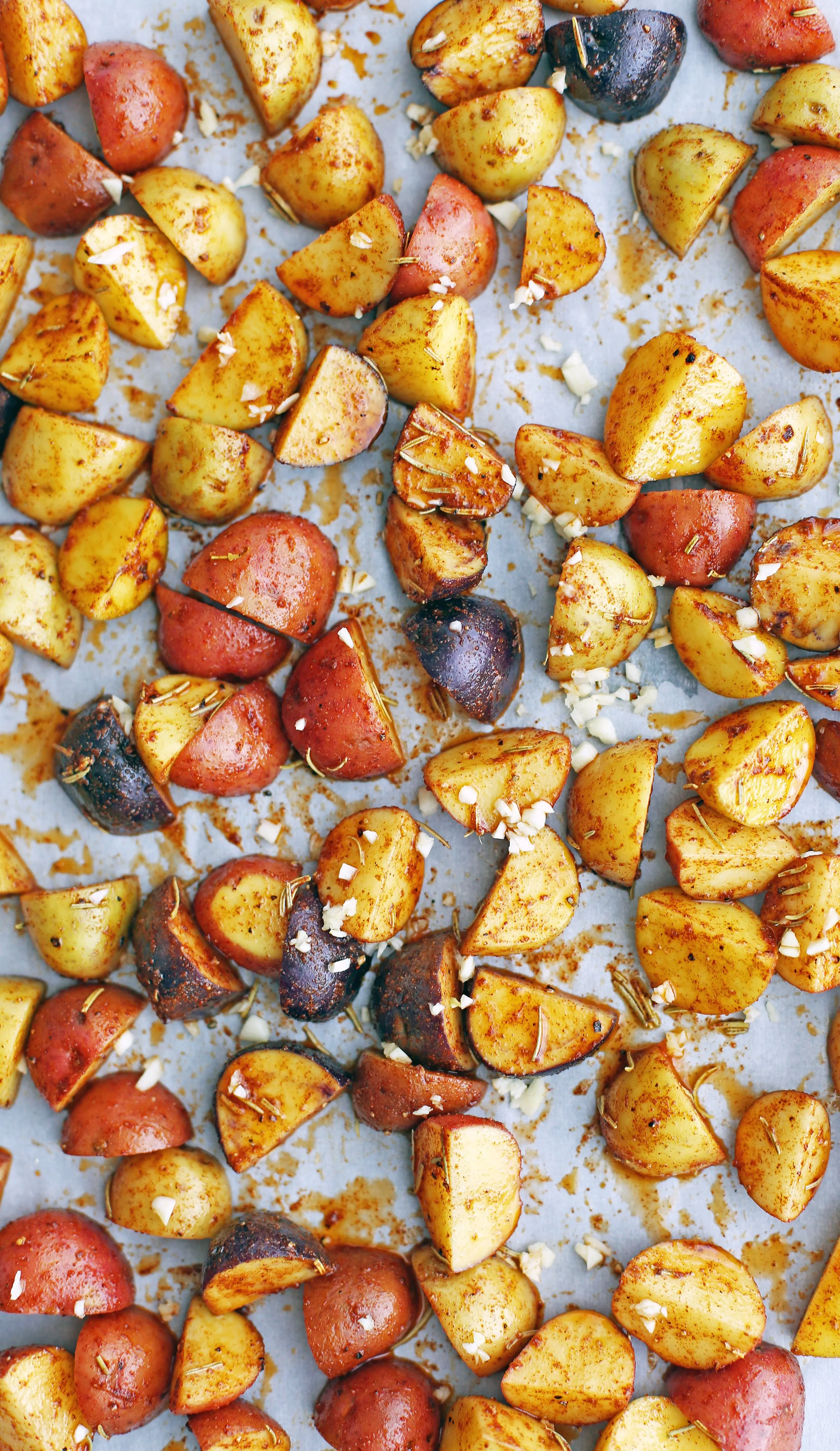 Chopped raw spiced baby potatoes on parchment paper lined baking sheet.