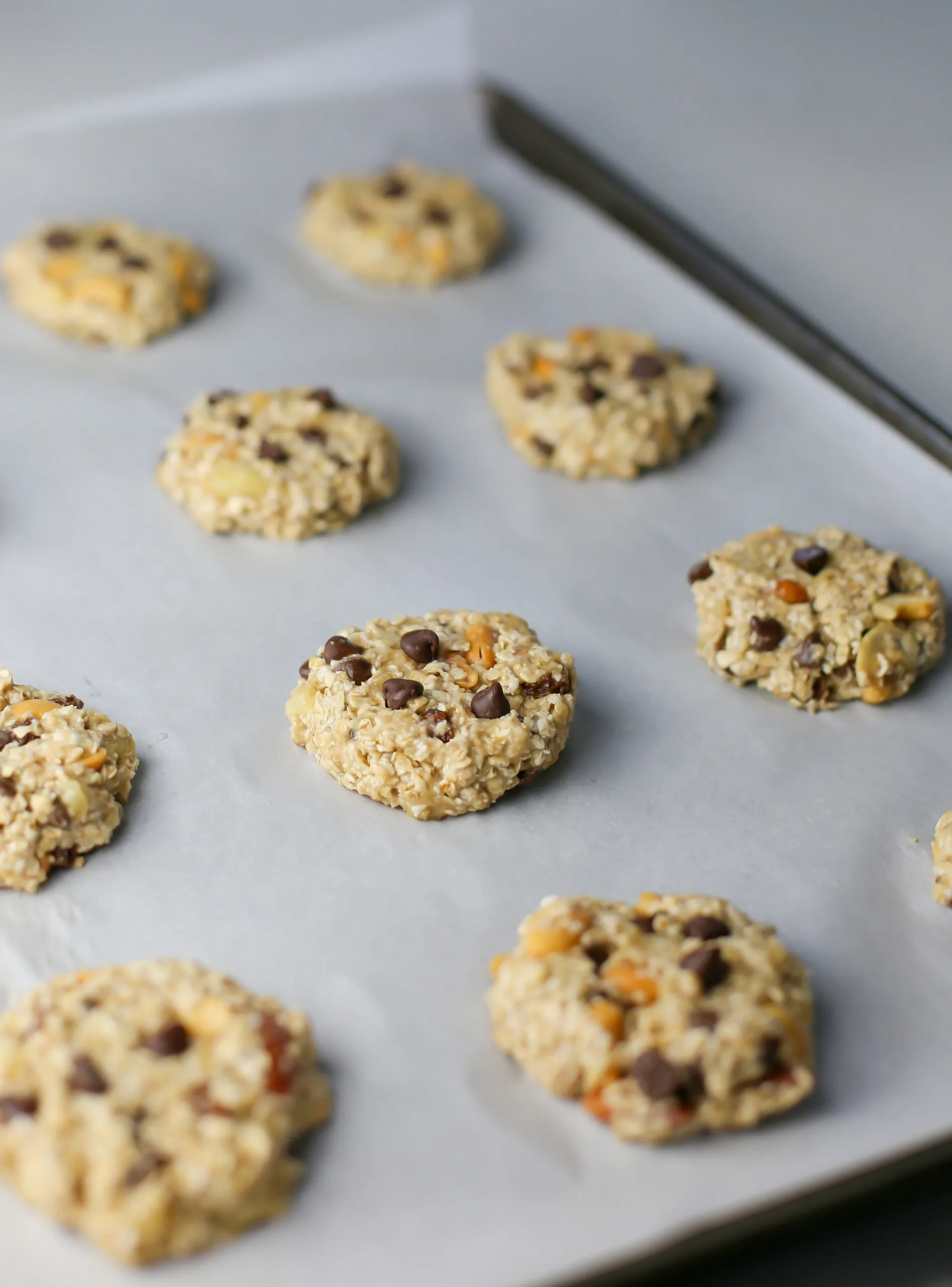 Unbaked trail mix cookies on a parchment paper lined baking sheet.