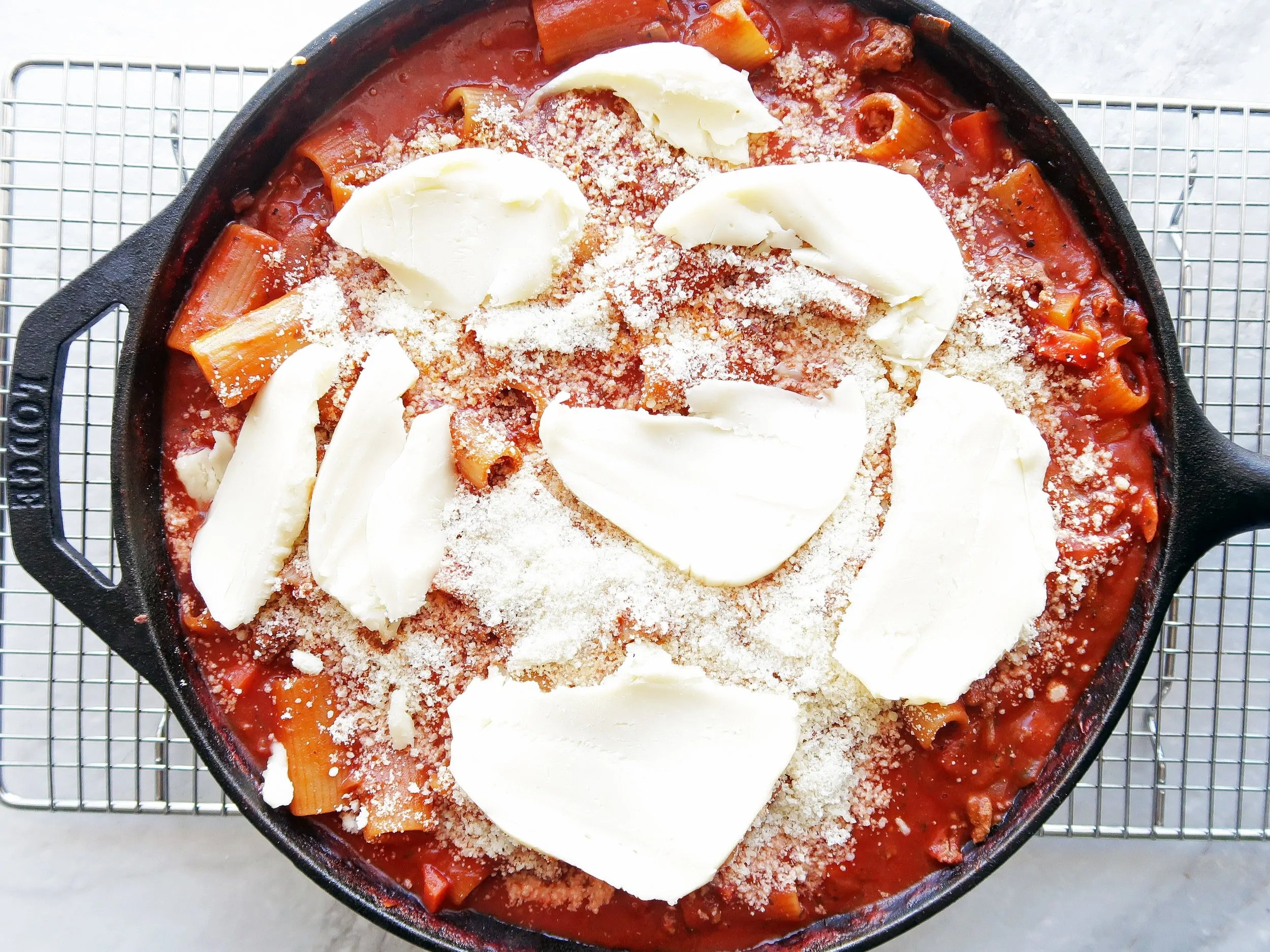 A cast iron skillet filled with rigatoni covered in meat sauce and topped with mozzarella and parmesan.