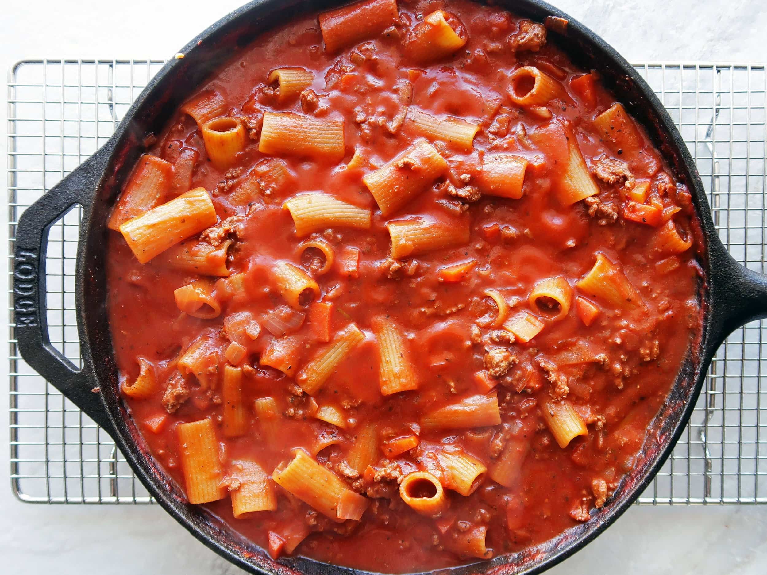A cast iron skillet full of rigatoni with covered in meat sauce.