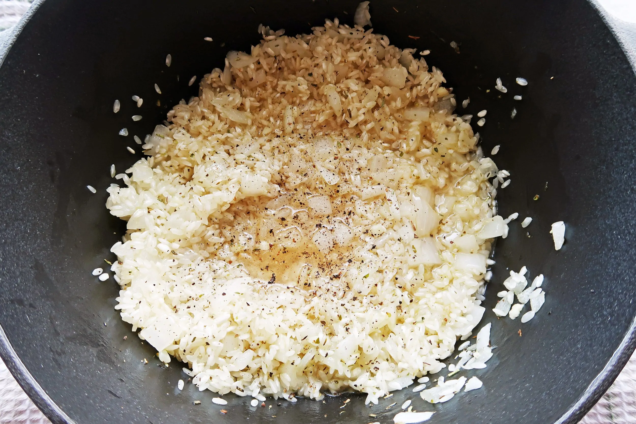 A Dutch oven containing arborio rice. onions, garlic, herbs,and white wine.