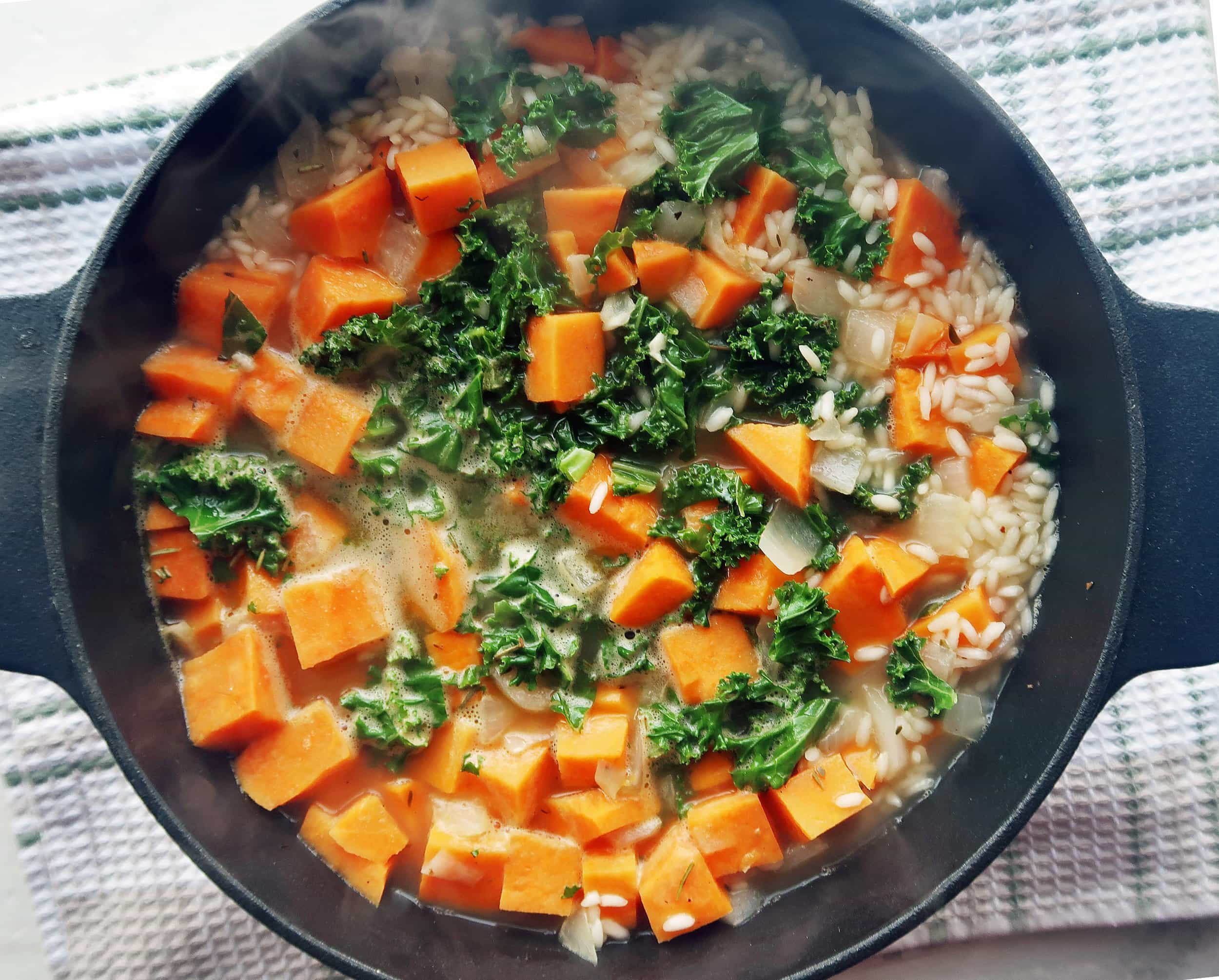 A Dutch oven full of sweet potato, kale, arborio rice, and vegetable broth.