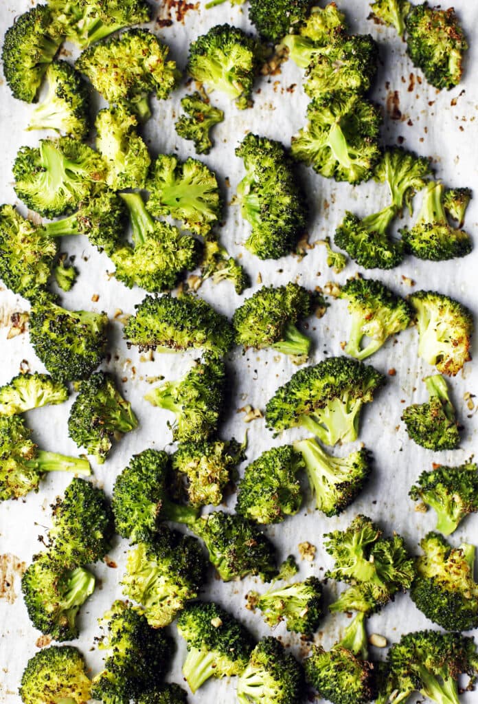 Roasted broccoli florets and minced garlic tossed in olive oil on parchment paper lined baking sheet.
