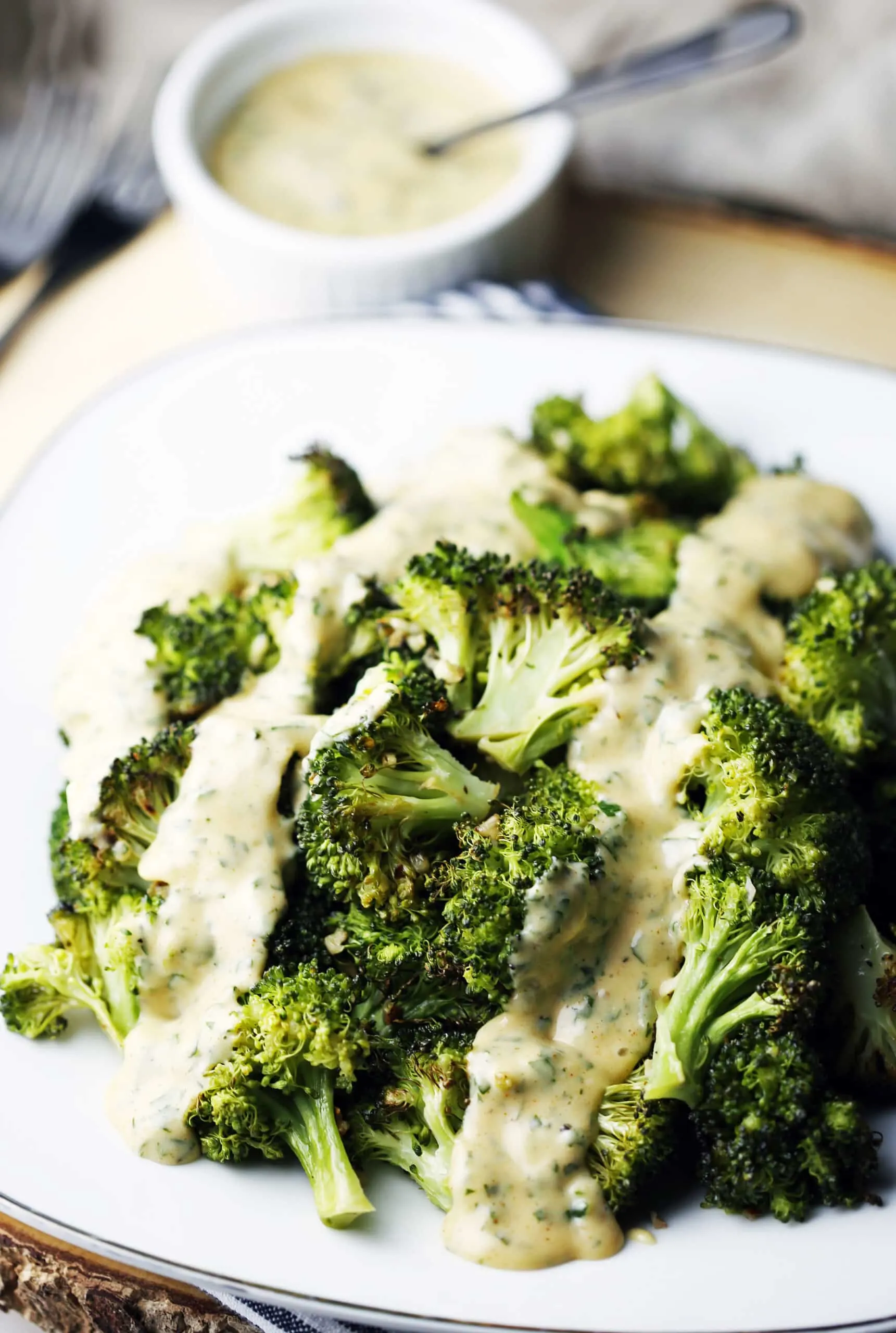 A side view of roasted broccoli topped with hollandaise sauce on a white plate.