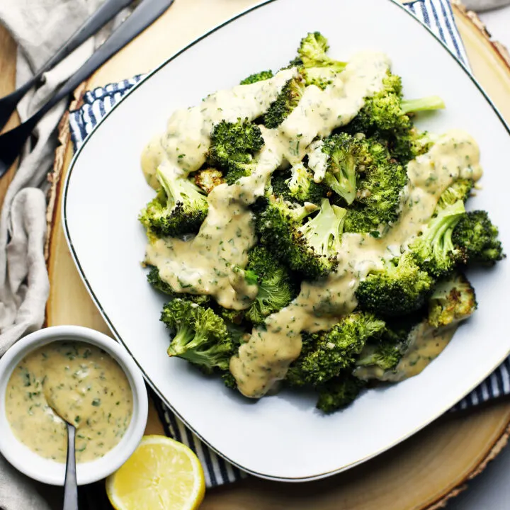 Overhead view of roasted broccoli with parsley lemon hollandaise sauce in white plate.