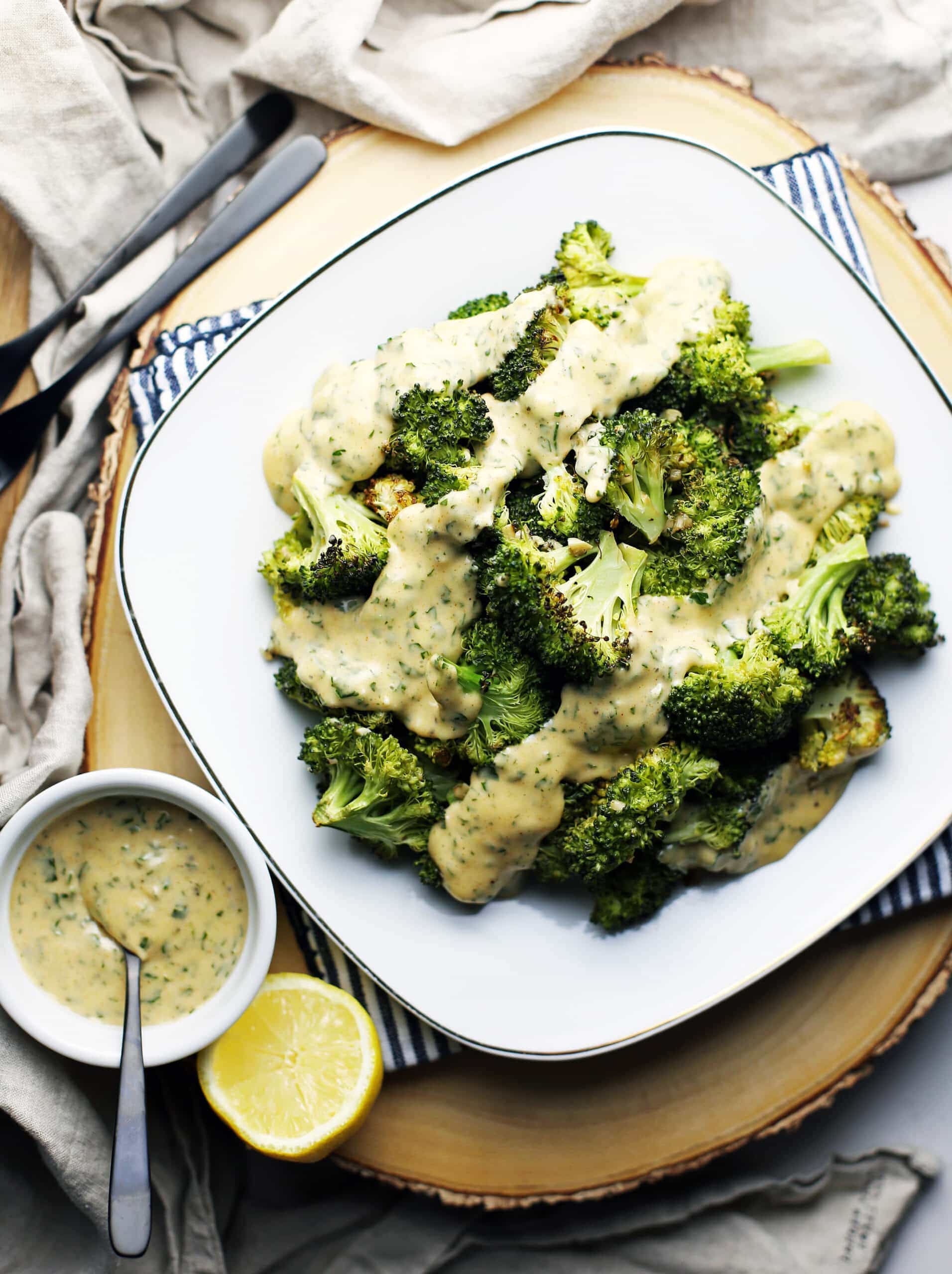 Overhead view of roasted broccoli with parsley lemon hollandaise sauce in white plate.