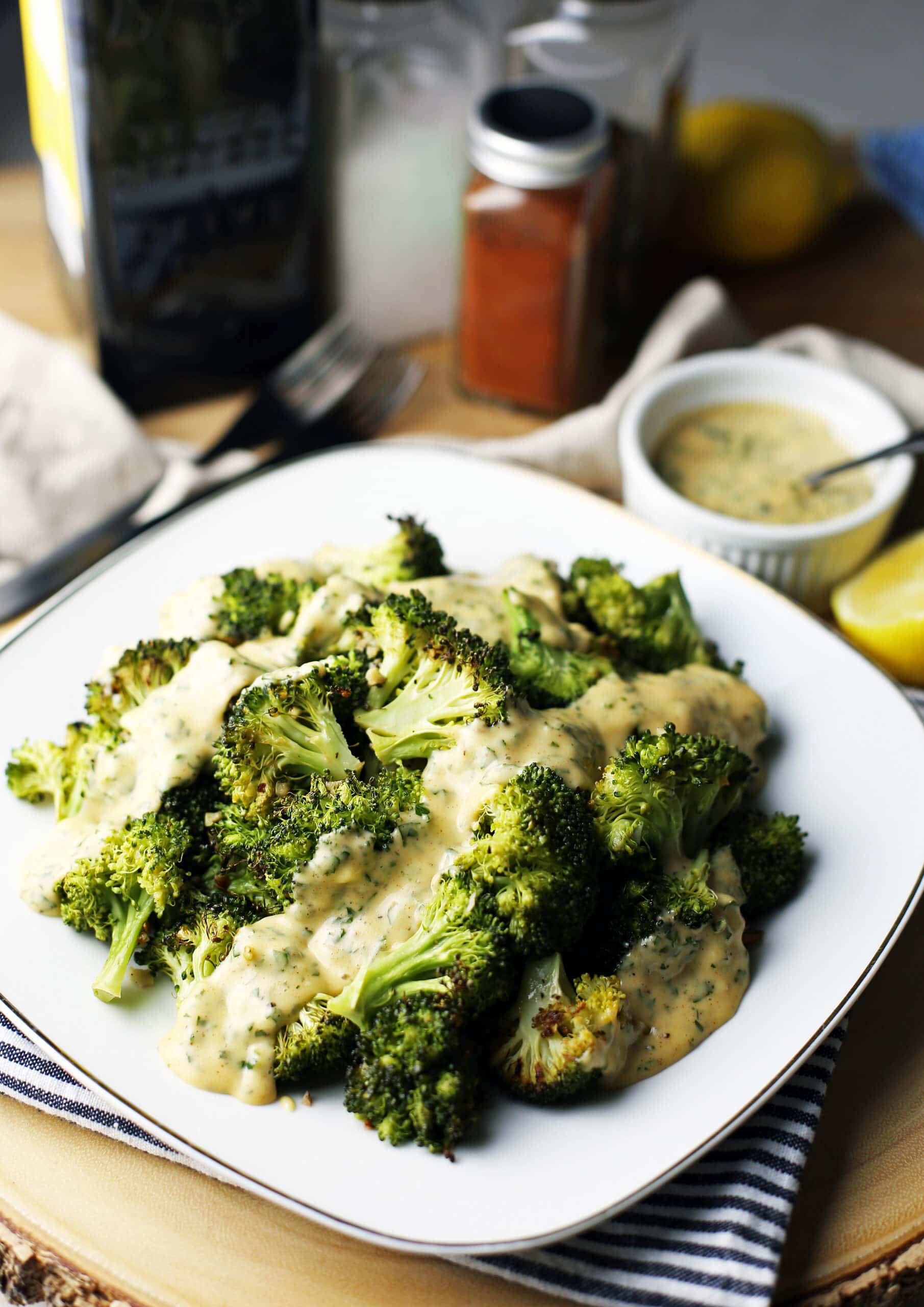 A square white plate with roasted broccoli topped with parsley lemon hollandaise sauce.