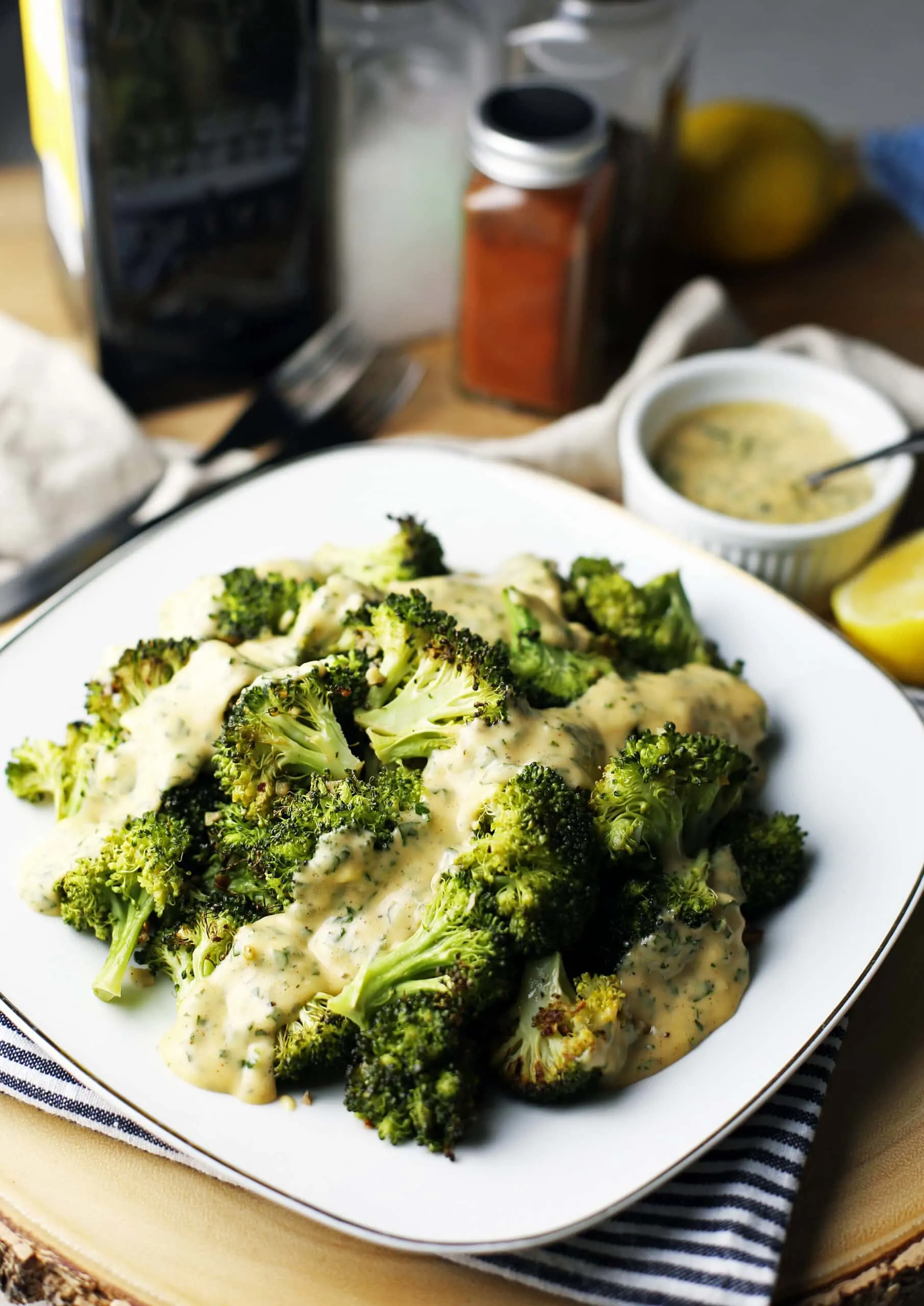 A square white plate with roasted broccoli topped with parsley lemon hollandaise sauce.