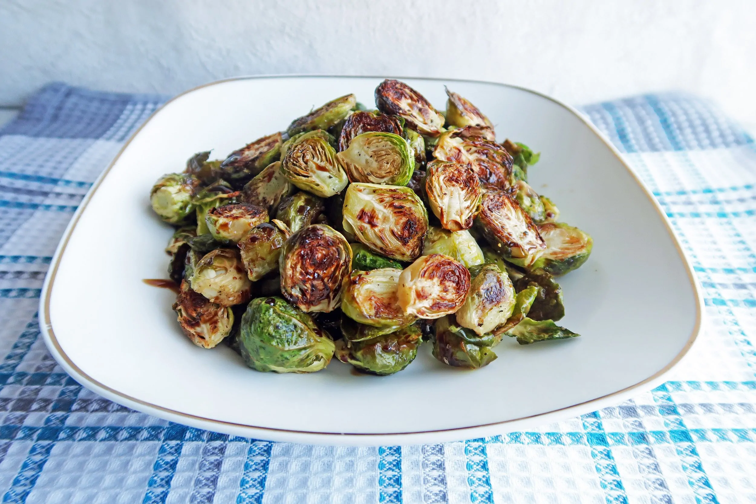 Side view of gluten-free and vegan Roasted Brussels Sprouts with Balsamic-Maple Glaze on a white plate.