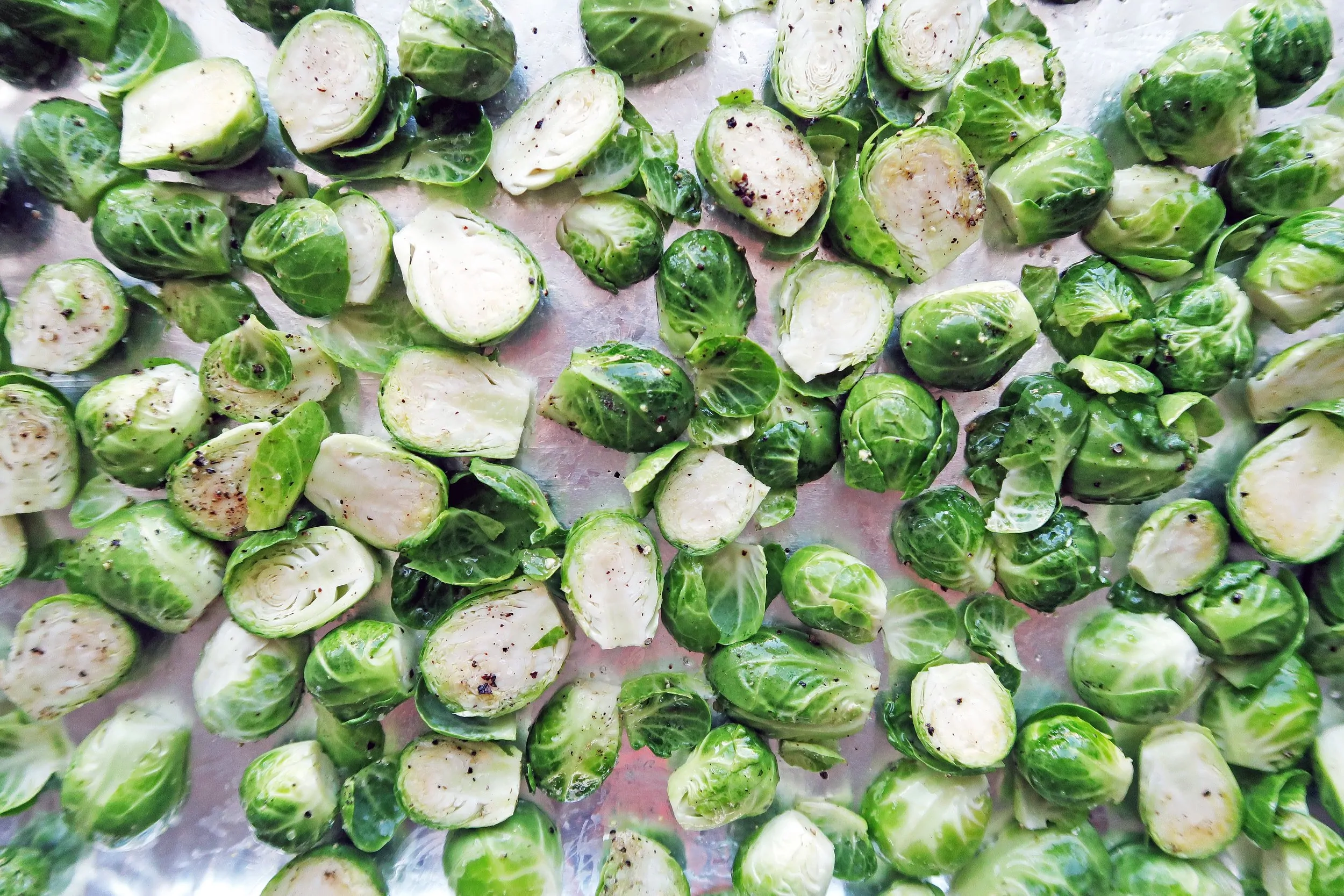 Brussels sprouts cut in half and seasoned with olive oil, salt, and pepper on a baking sheet.