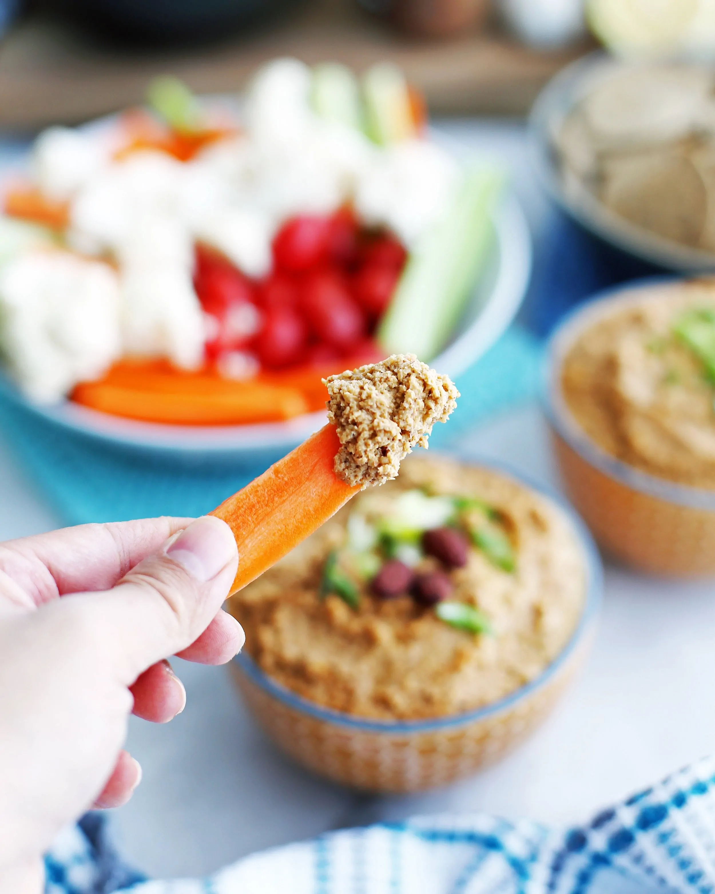 Close-up view of a hand holding a carrot stick that has been dipped in spicy roasted cauliflower garlic dip.