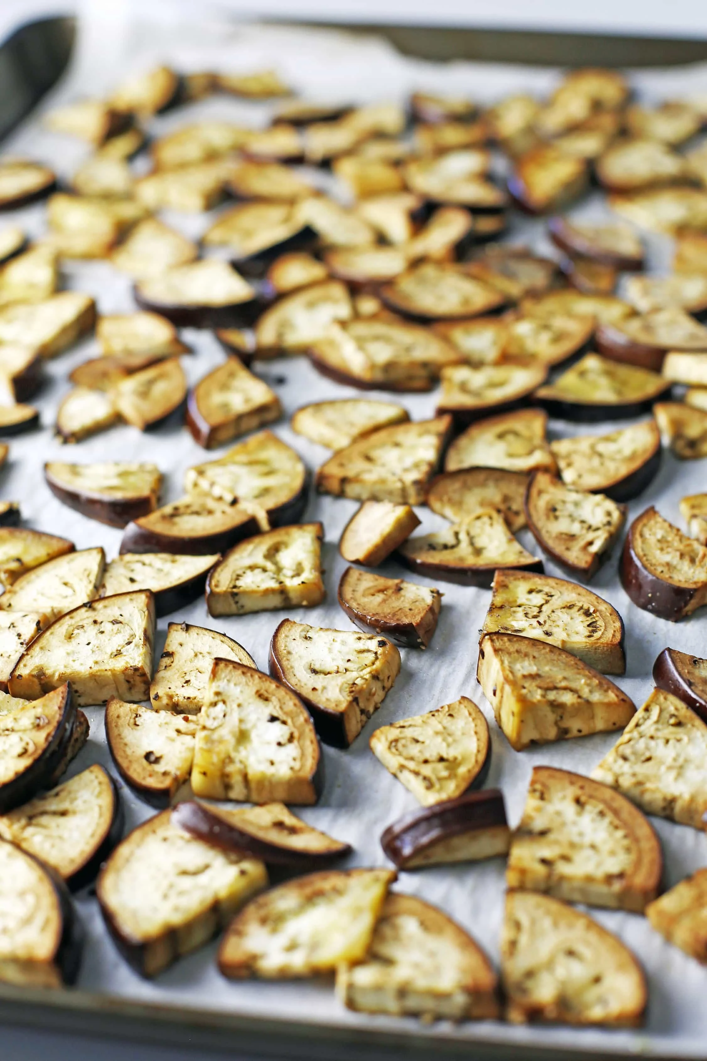 Lightly roasted sliced Italian eggplant on a large baking sheet lined with parchment paper.