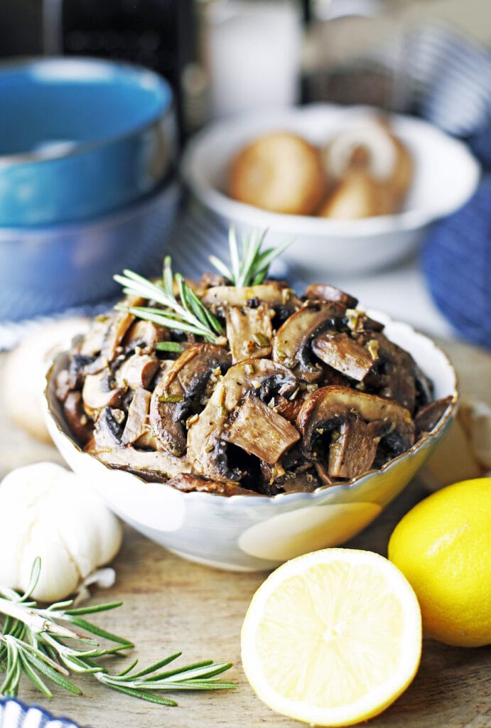 A blue and white bowl filled with roasted lemon garlic mushroom with a sprig of rosemary on top.