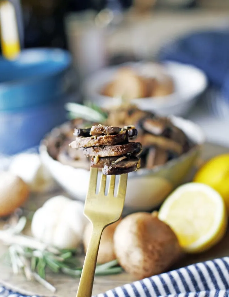 A closeup of a gold fork holding slices of roasted lemon garlic mushrooms.