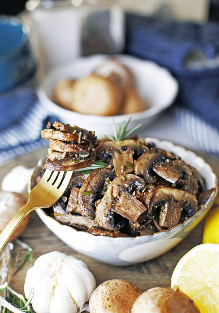 A bowl of roasted lemon garlic mushroom with a fork holding more roasted mushrooms on the side.
