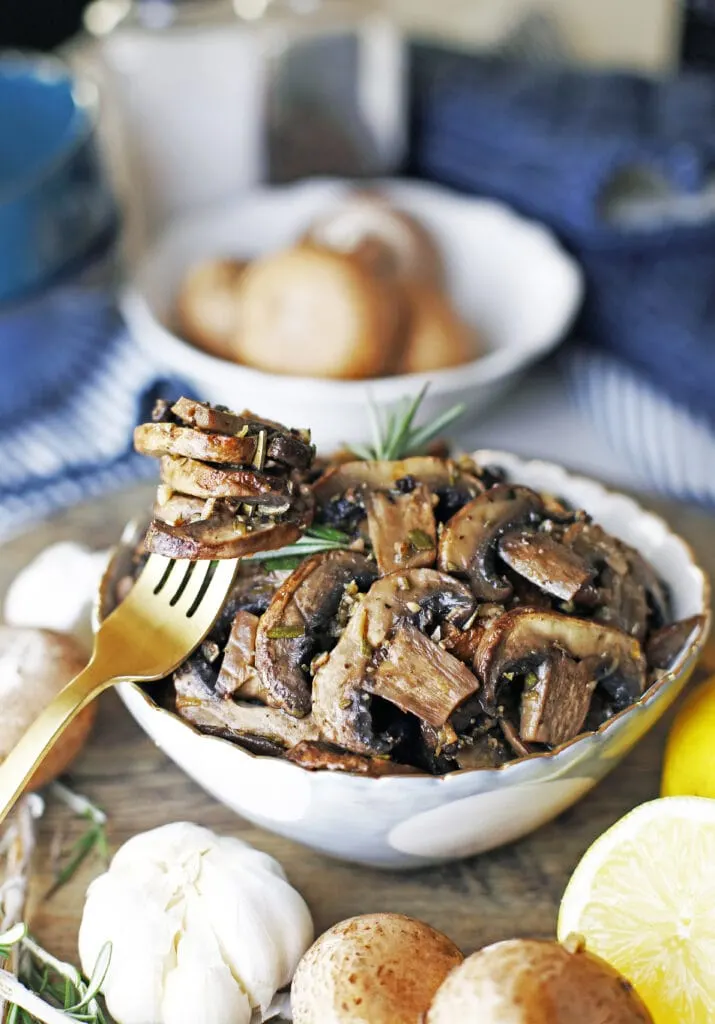 A bowl of roasted lemon garlic mushroom with a fork holding more roasted mushrooms on the side.