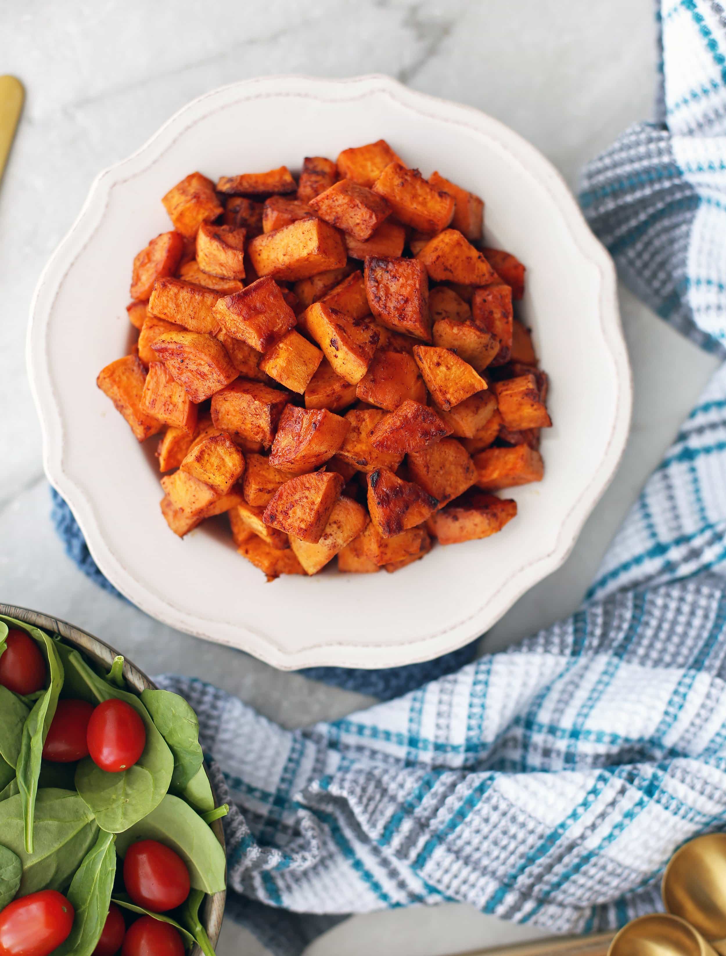 Overhead view of a white bowl containing roasted maple cinnamon sweet potatoes piled high.