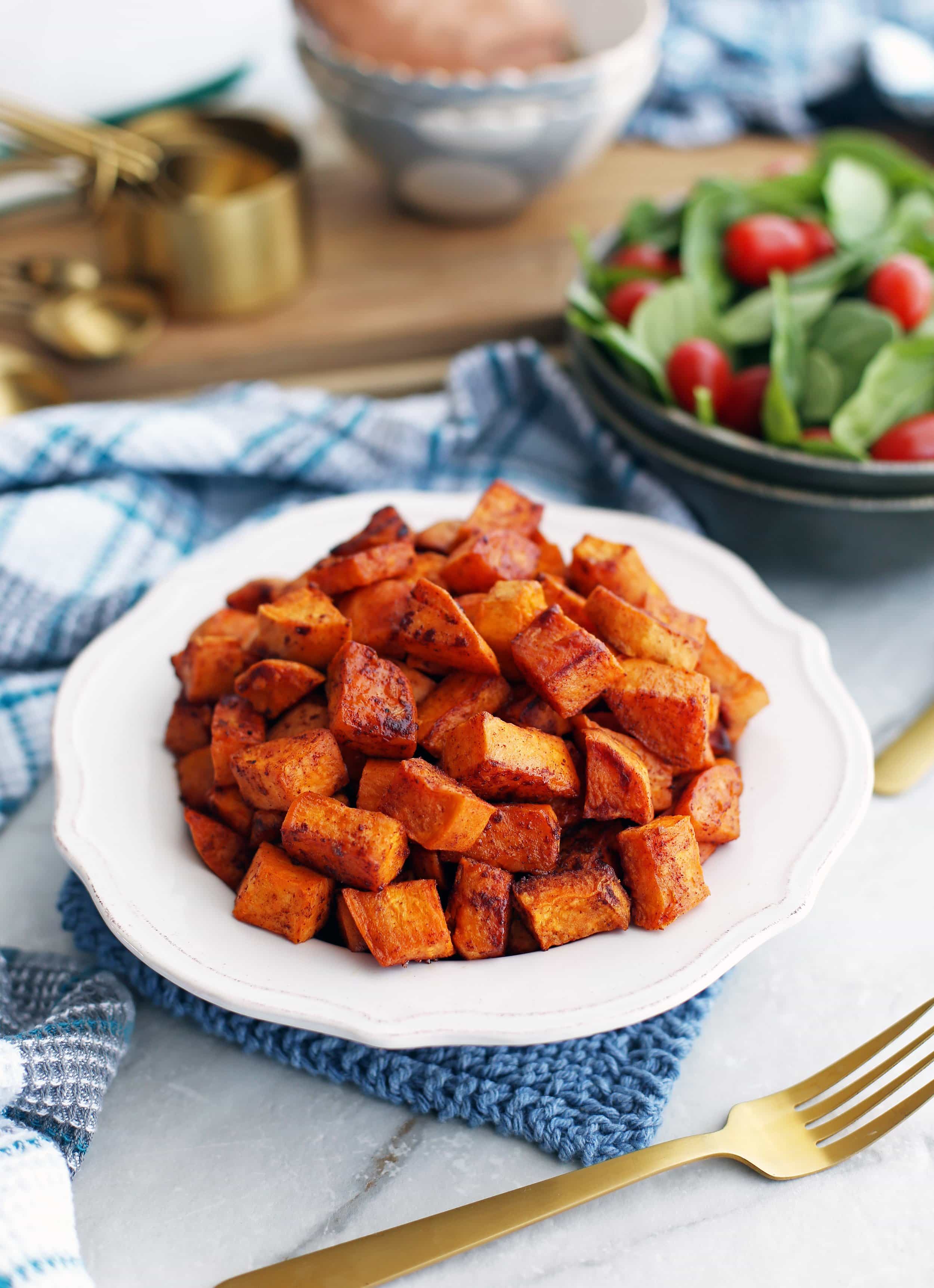 Bite-sized roasted maple cinnamon sweet potatoes piled in a white bowl with a fork to its side.