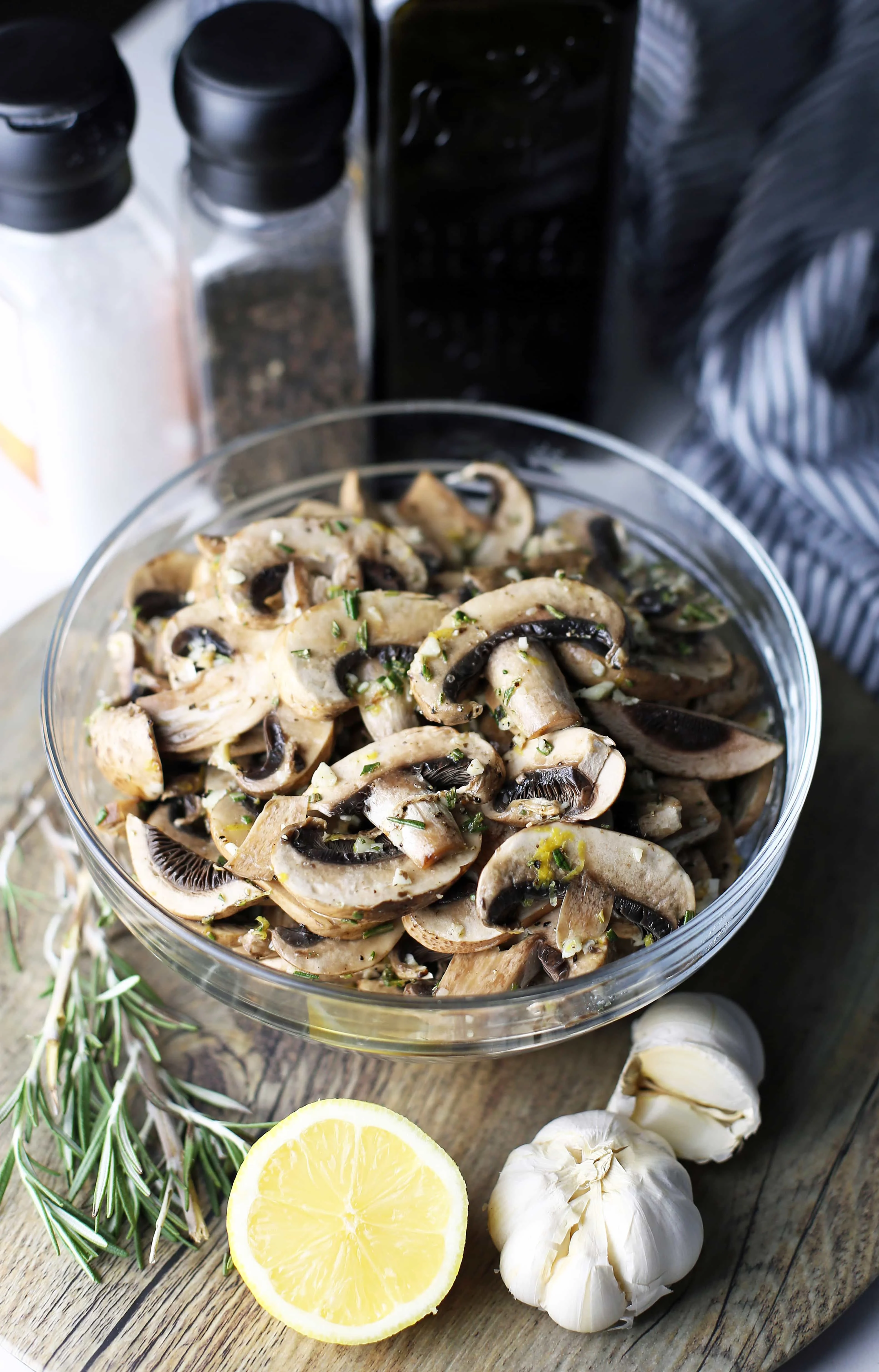 A bowl of sliced cremini mushrooms with garlic, lemon juice and zest, rosemary, and olive oil.