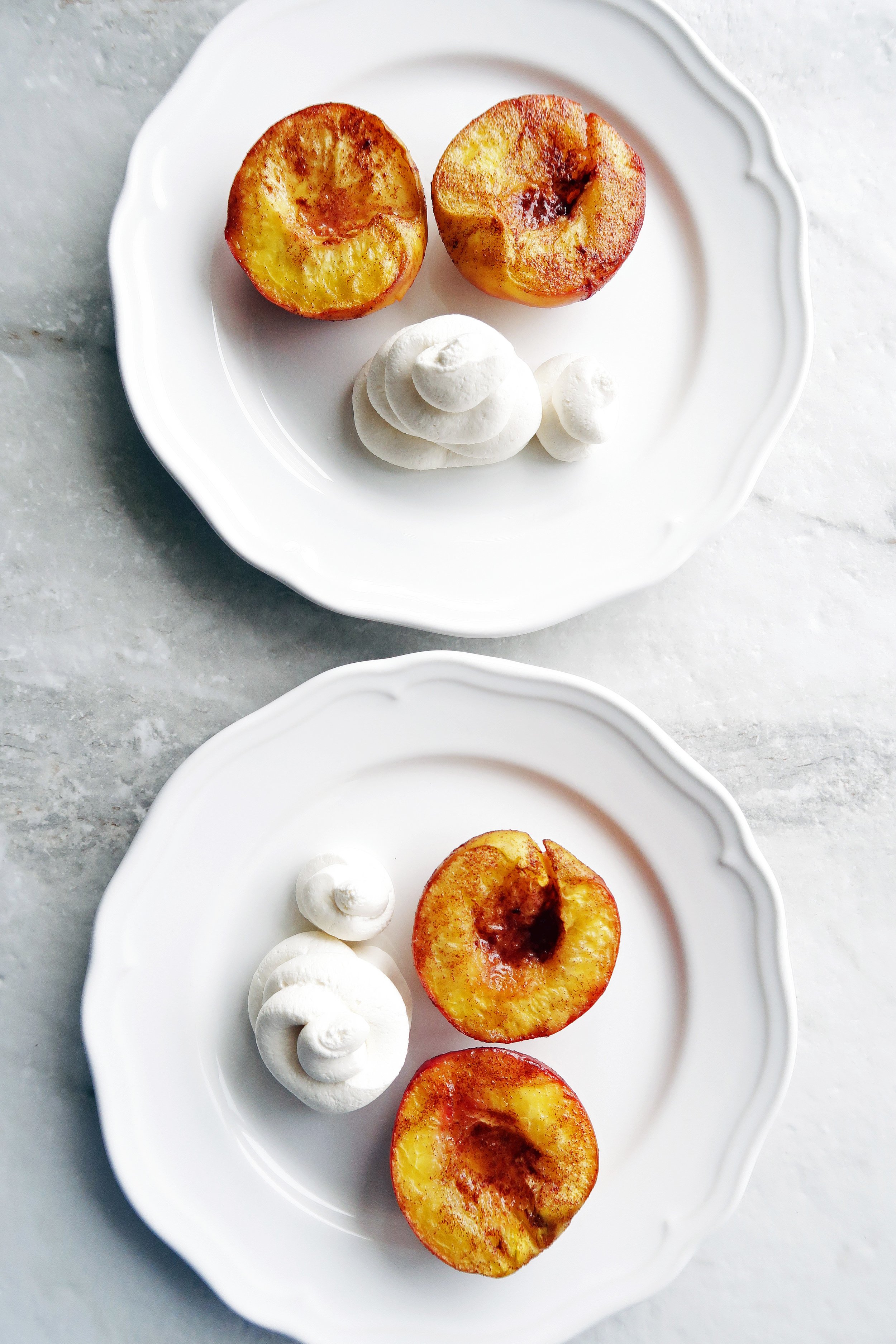 Cinnamon Roasted Peach Halves with Honey Mascarpone Whipped Cream beside the peaches on two white plates.