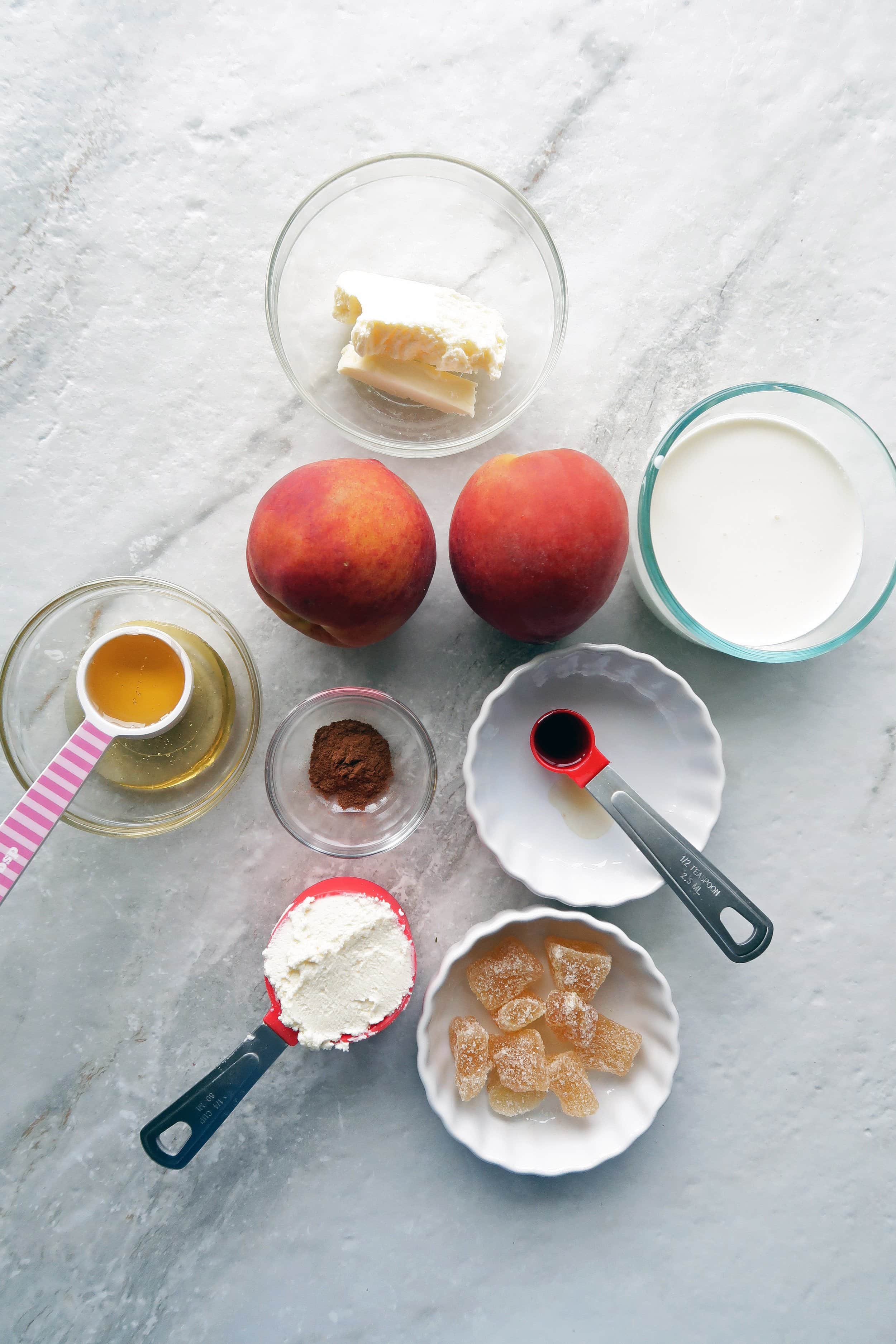 Two peaches surrounded by bowls of butter, cream, honey, marscarpone, vanilla, cinnamon, and candied ginger.