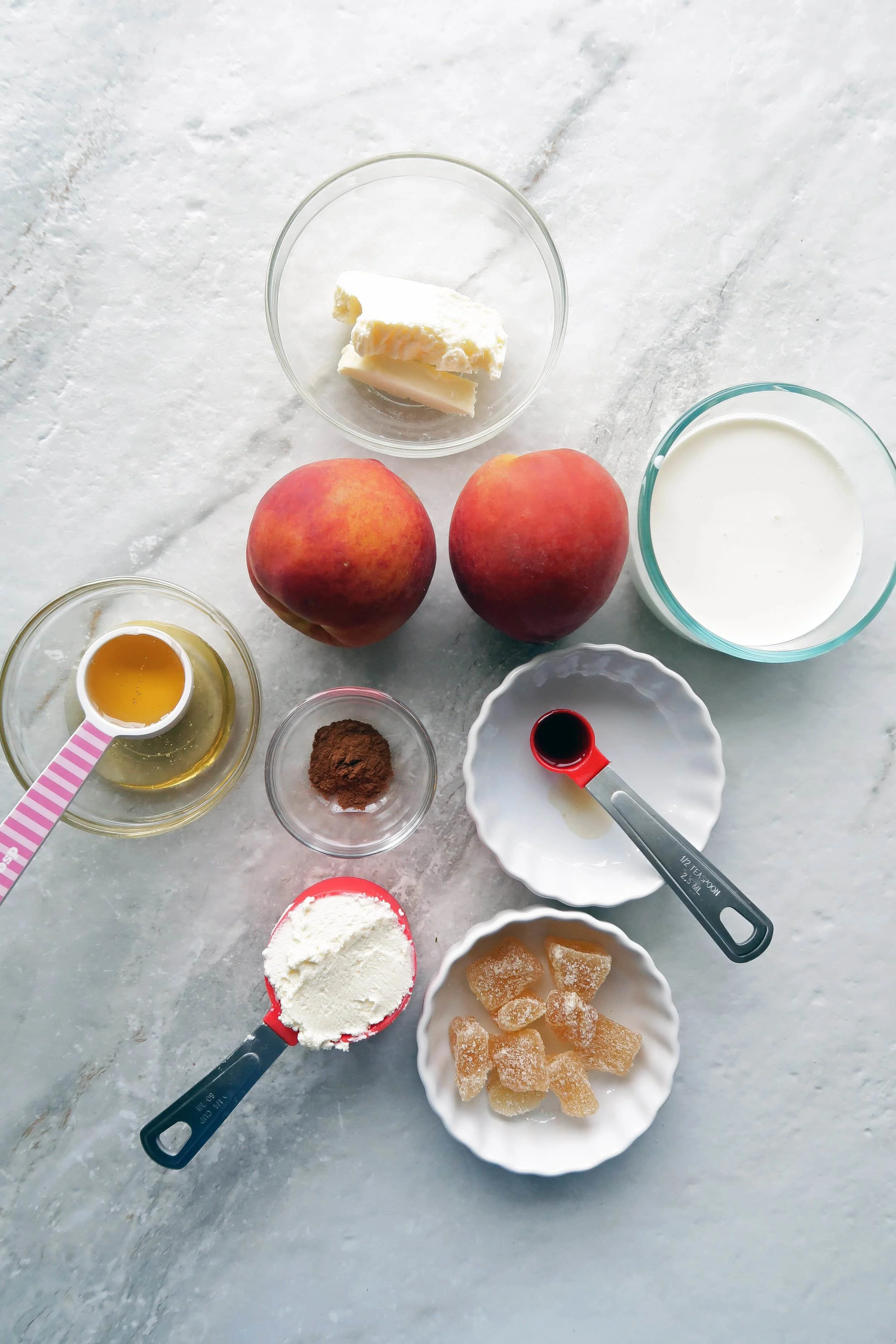 Two peaches surrounded by bowls of butter, cream, honey, marscarpone, vanilla, cinnamon, and candied ginger.