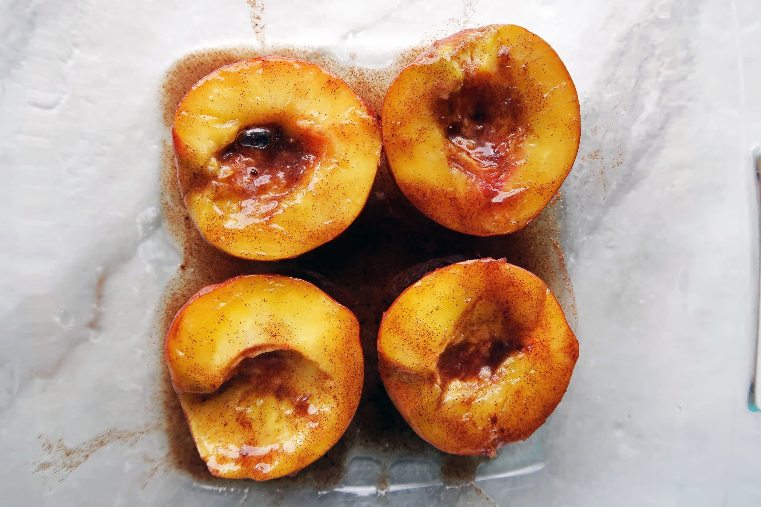 Four peach halves face up in a baking dish and covered with honey, cinnamon, and butter.