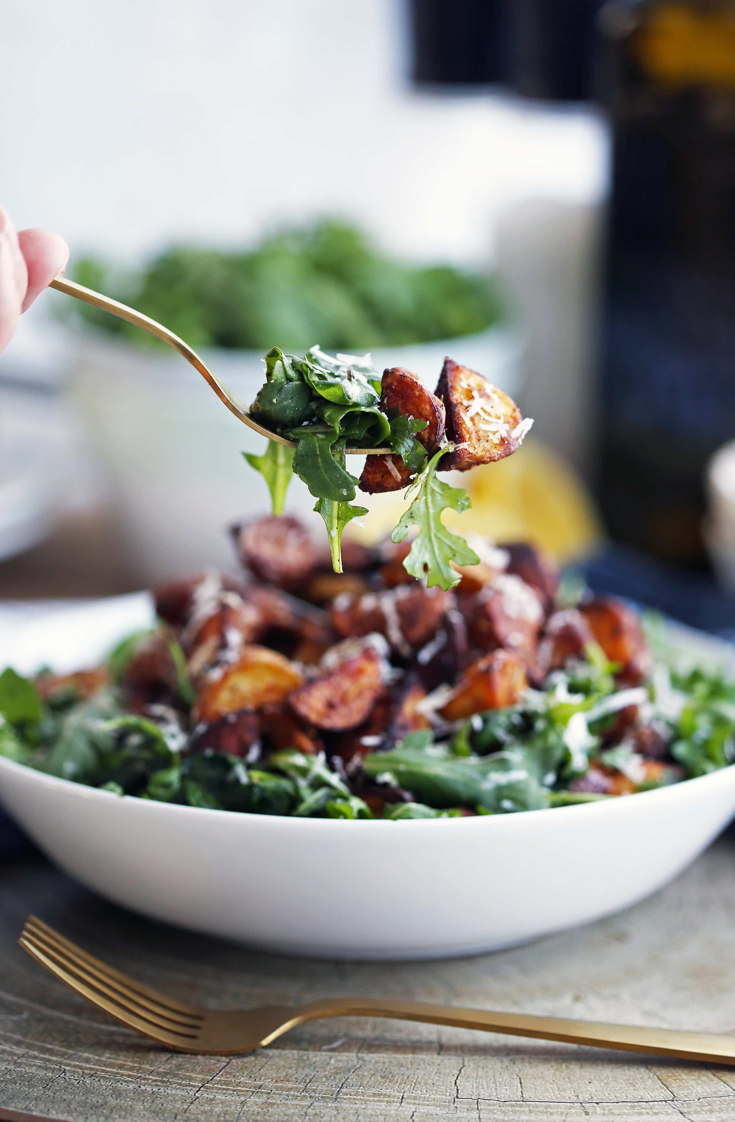 A fork holding roasted baby potato and baby arugula over a full bowl containing more of the same salad.