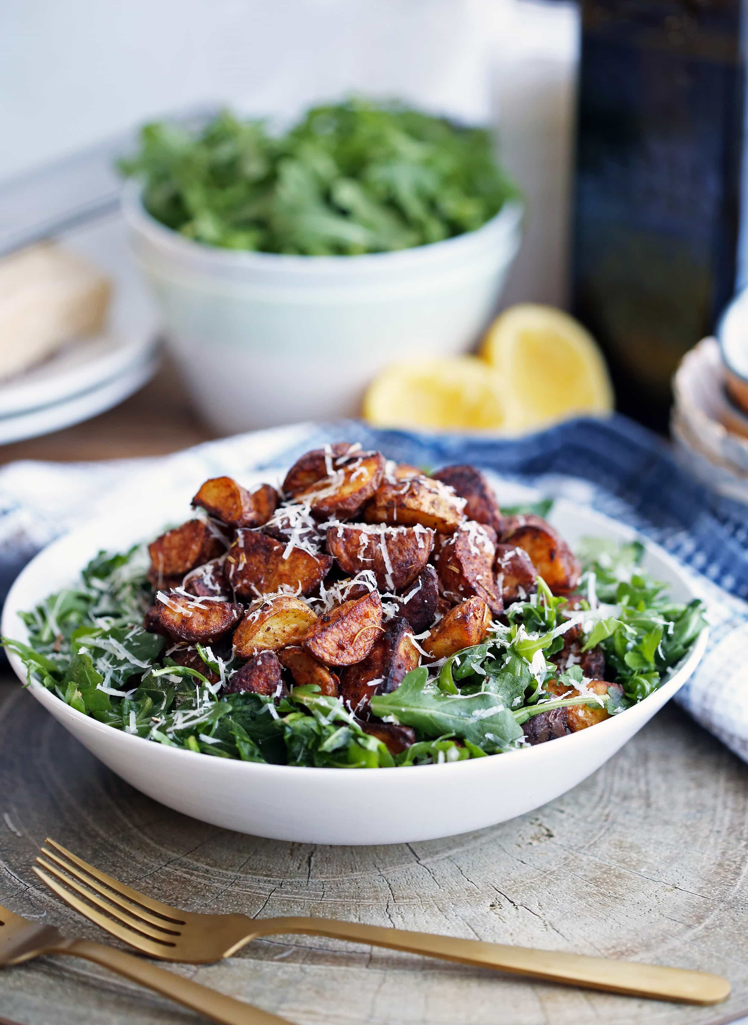 Crispy roasted spiced baby potato and arugula salad topped with parmesan cheese in a large white bowl.