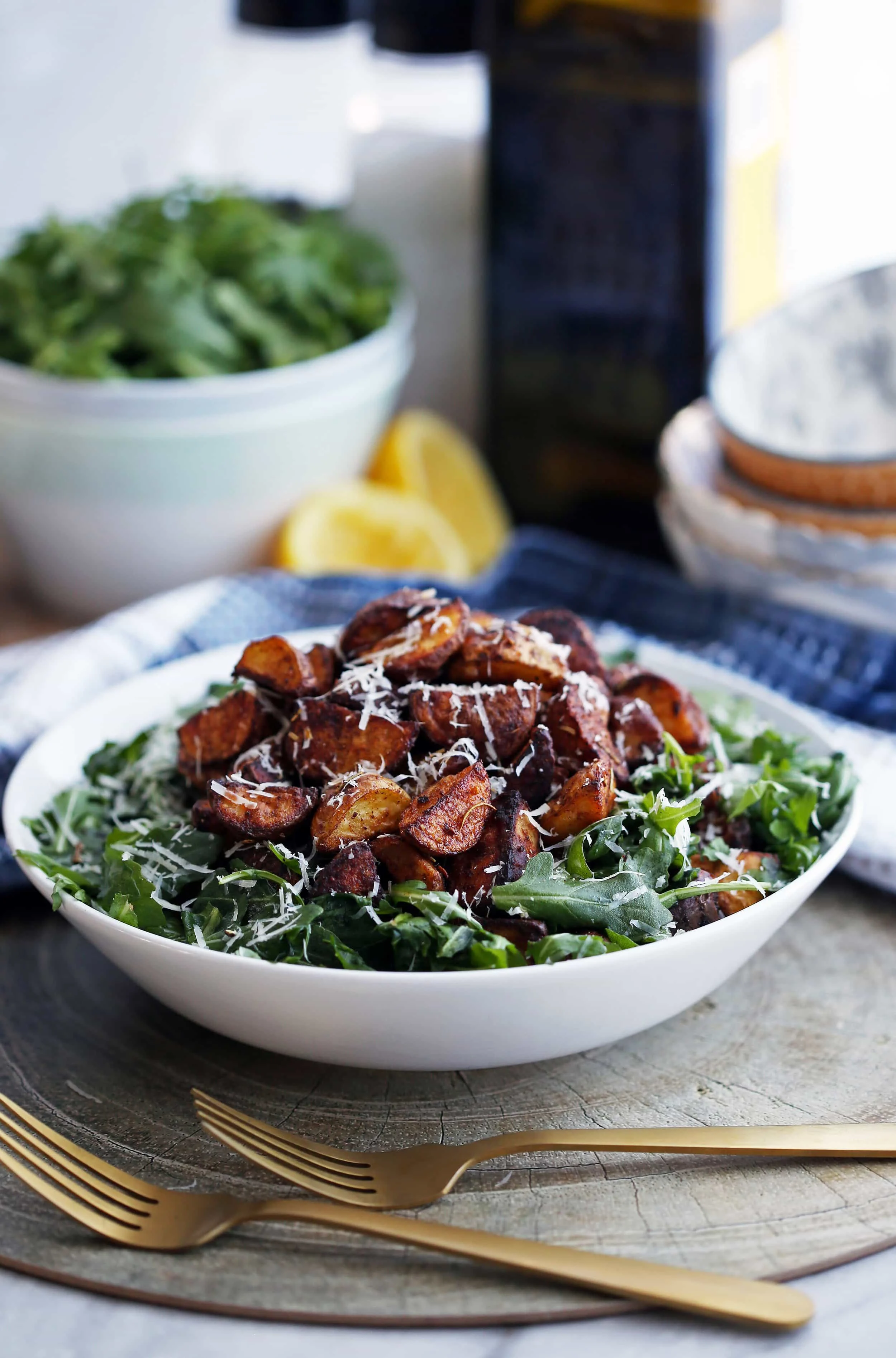 A wide white bowl full of crispy roasted potato and arugula salad that’s sprinkled with parmesan cheese.