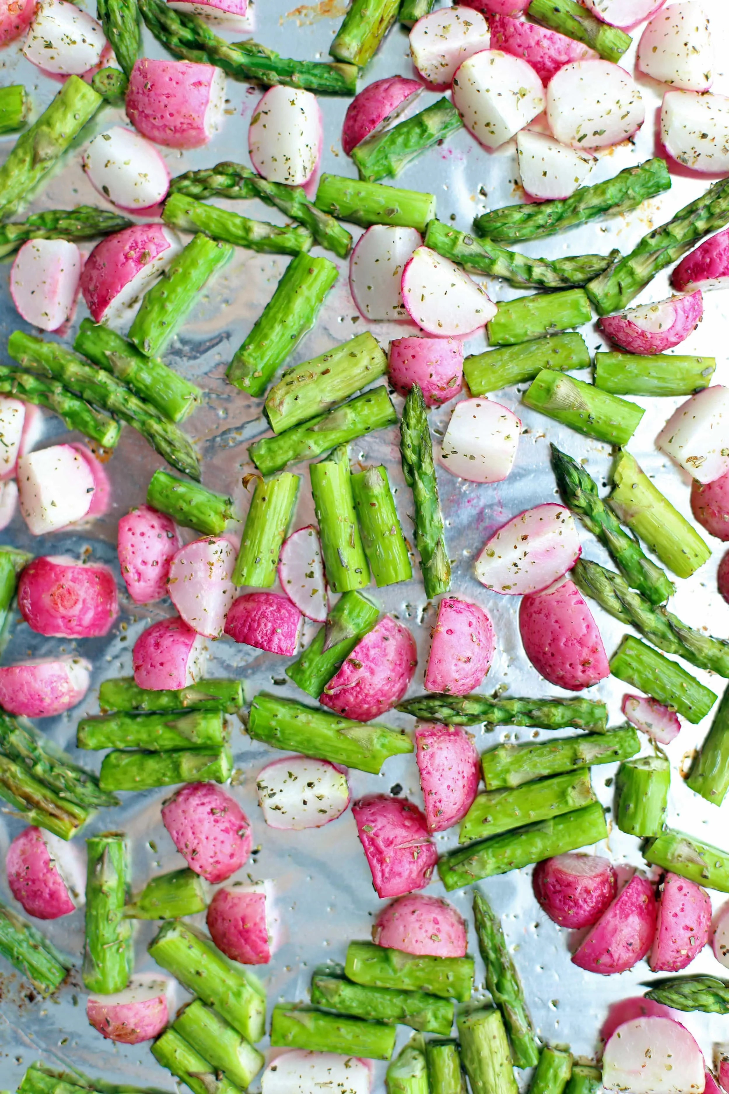 Roasted chopped asparagus and radishes on a baking sheet.