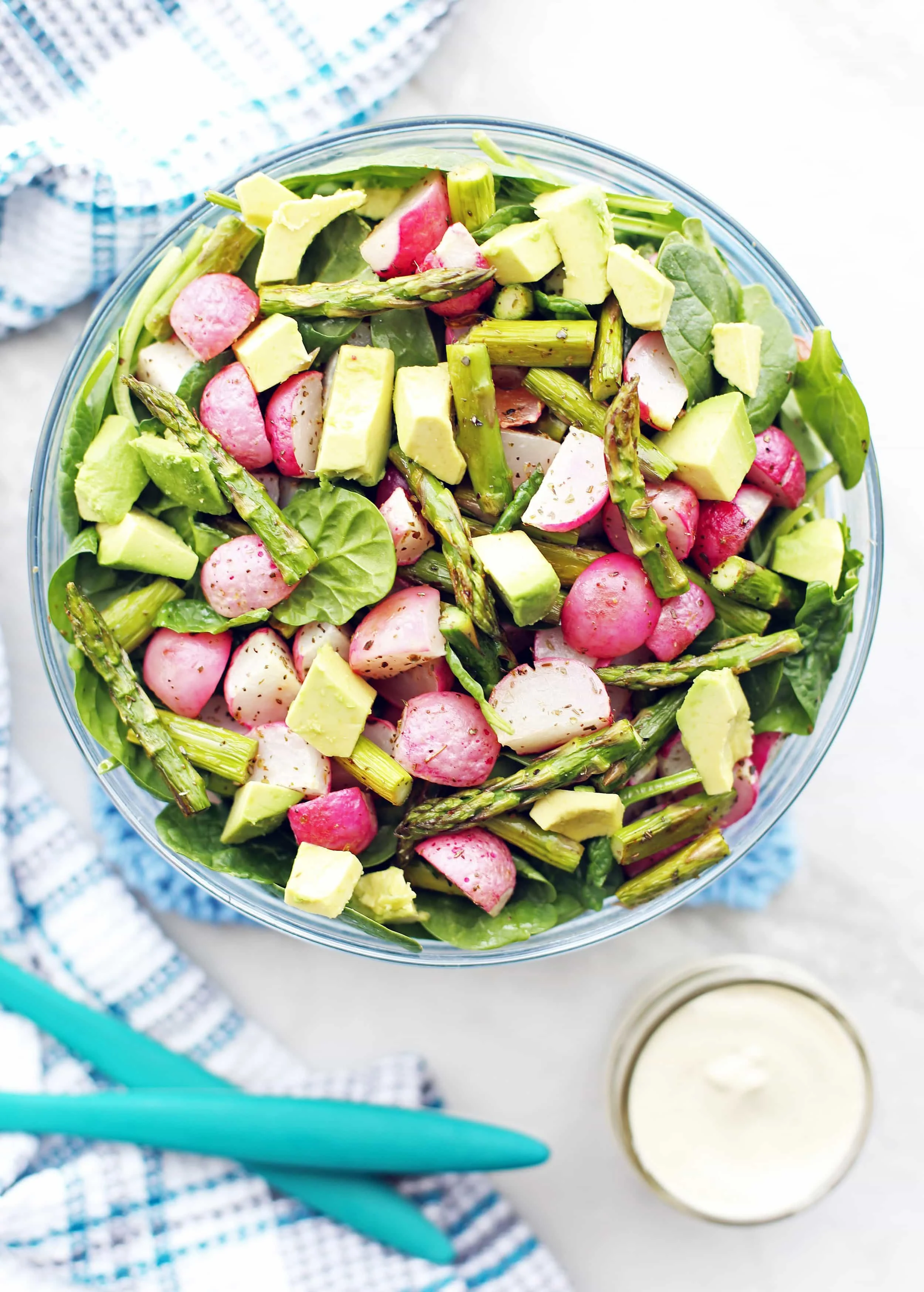 Overhead view of Roasted Asparagus and Radish Salad with spinach and avocado in a large glass bowl.