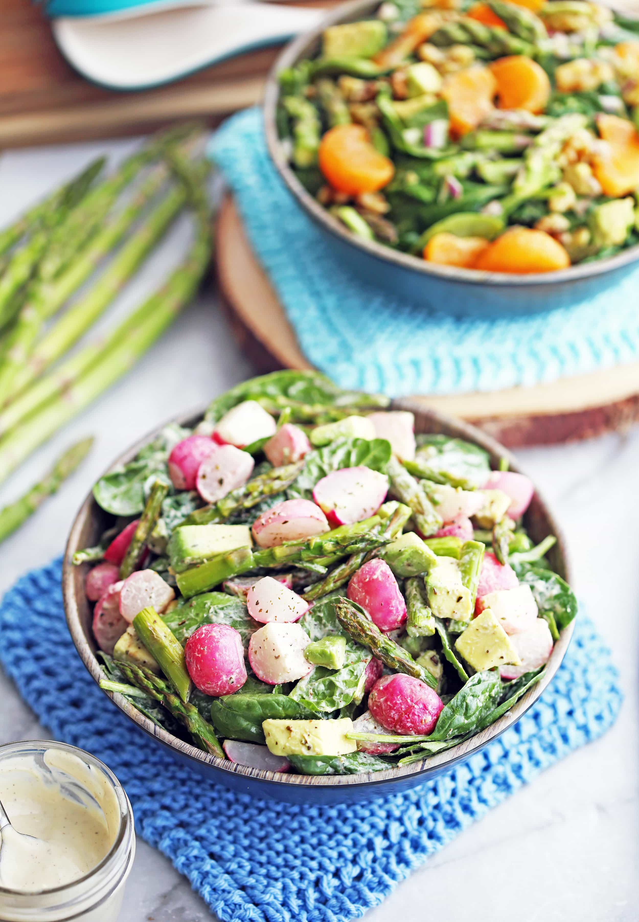 A wooden bowl of Roasted Asparagus and Radish Salad with a small jar of garlic cashew dressing to its side.