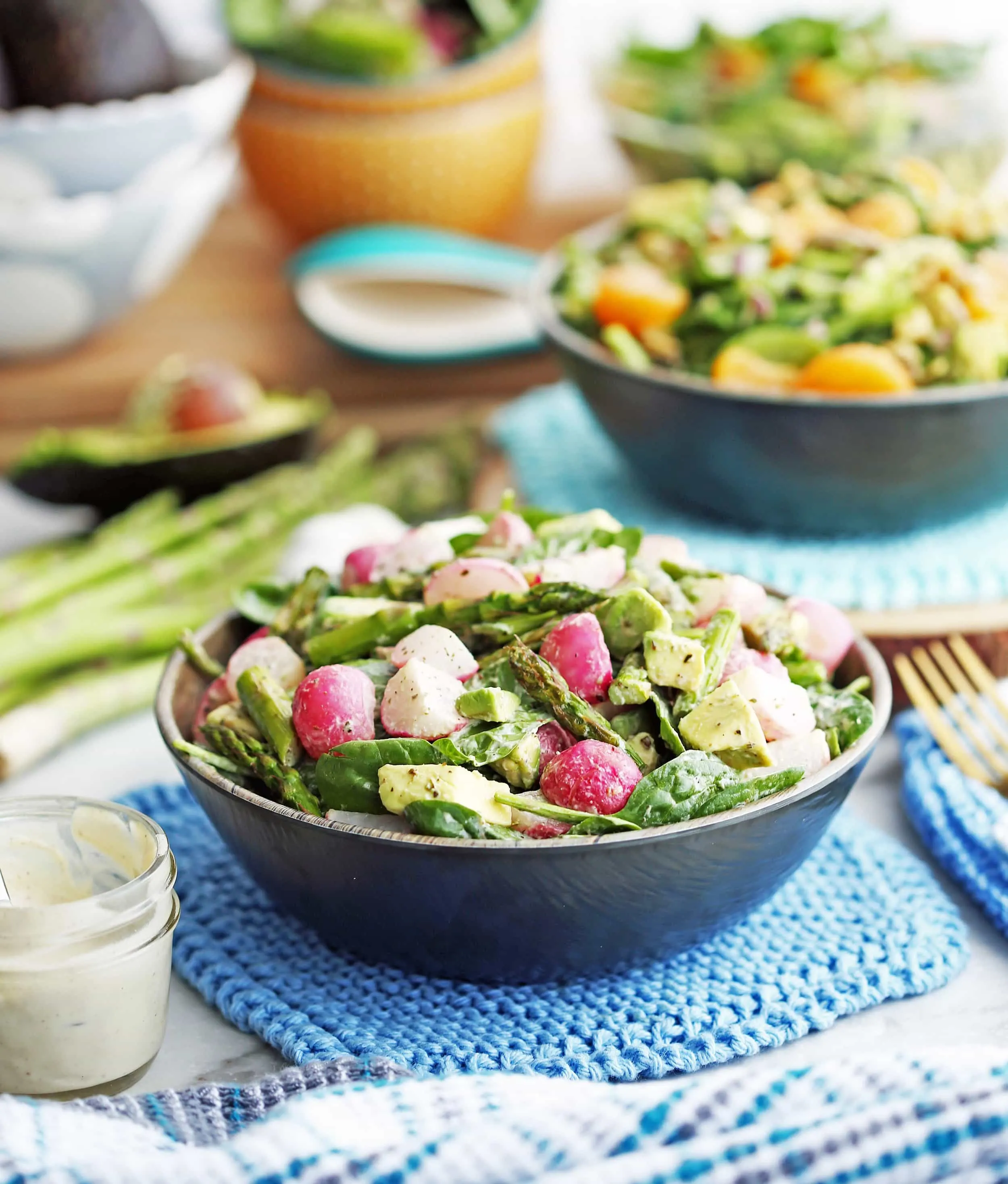 Roasted Asparagus and Radish Salad with Creamy Garlic Cashew Dressing in a wooden bowl with more dressing to its side.