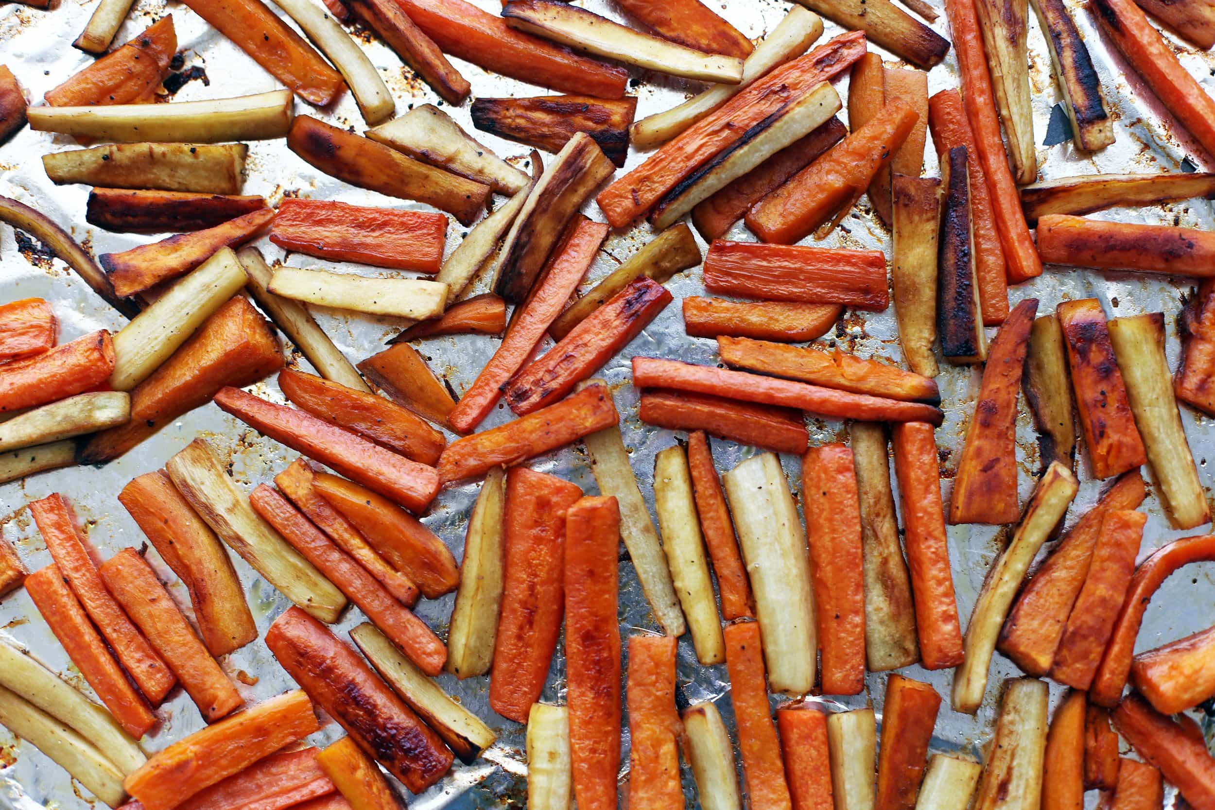 Roasted carrots, parsnips, and sweet potatoes in a single layer on an aluminum foiled lined baking sheet.