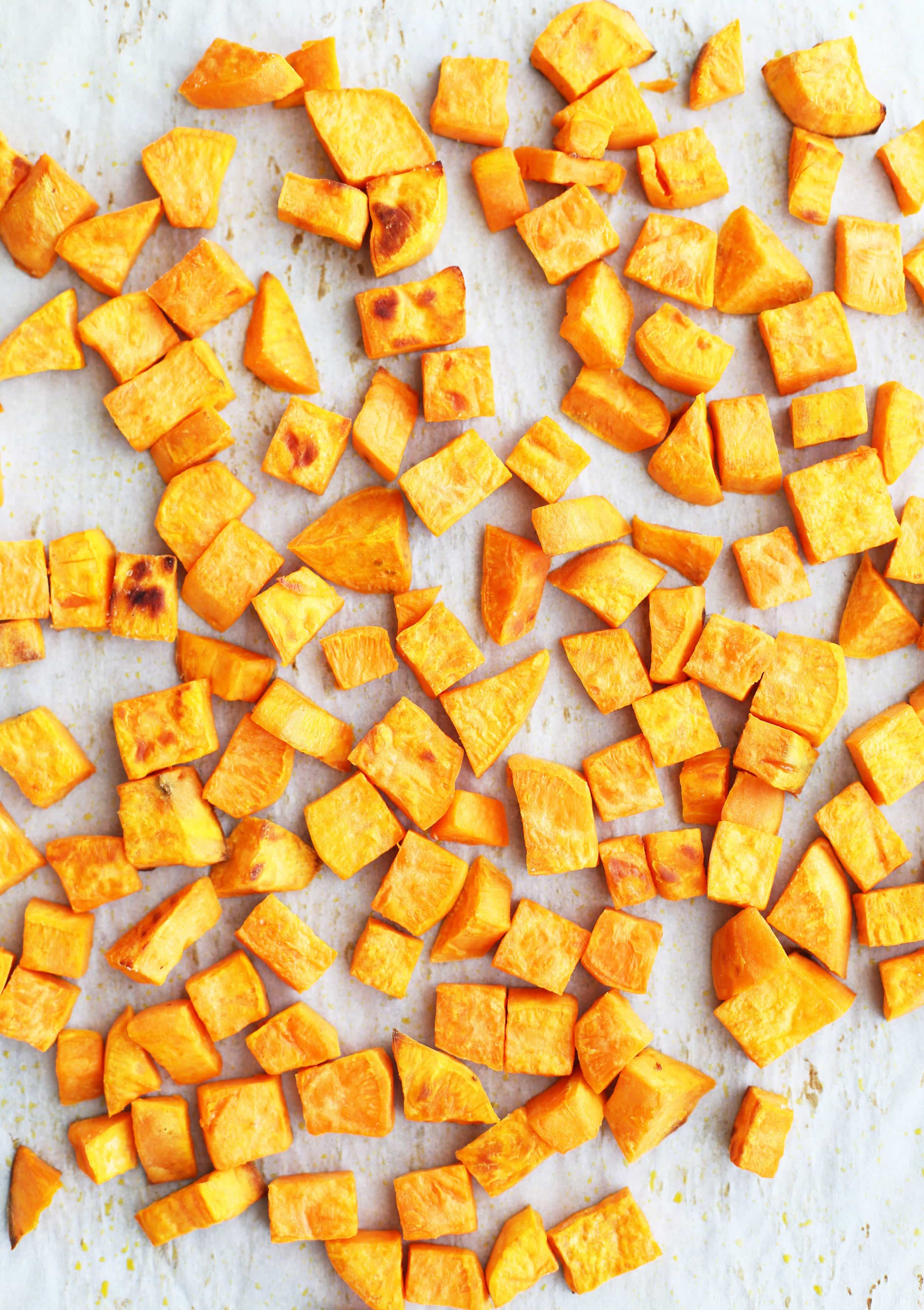 Roasted sweet potatoes pieces on a parchment paper lined baking sheet.