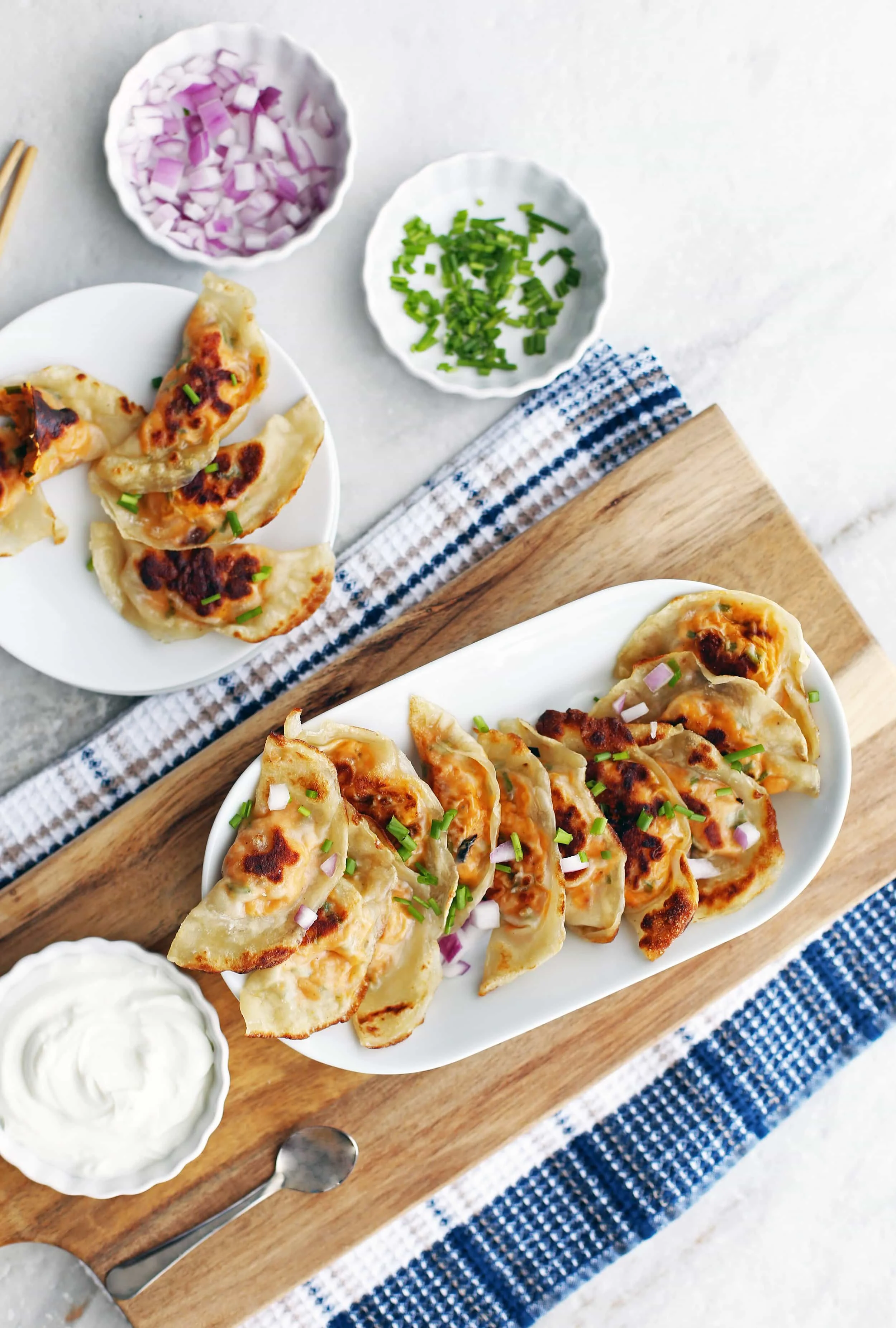 Sweet potato cream cheese potstickers on a long platter with a bowl of sour cream on the side.
