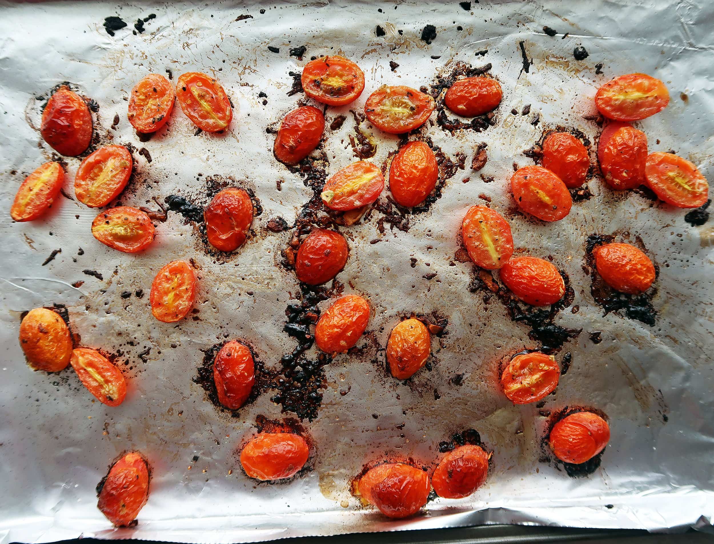 Roasted cherry tomatoes with garlic on a baking sheet.