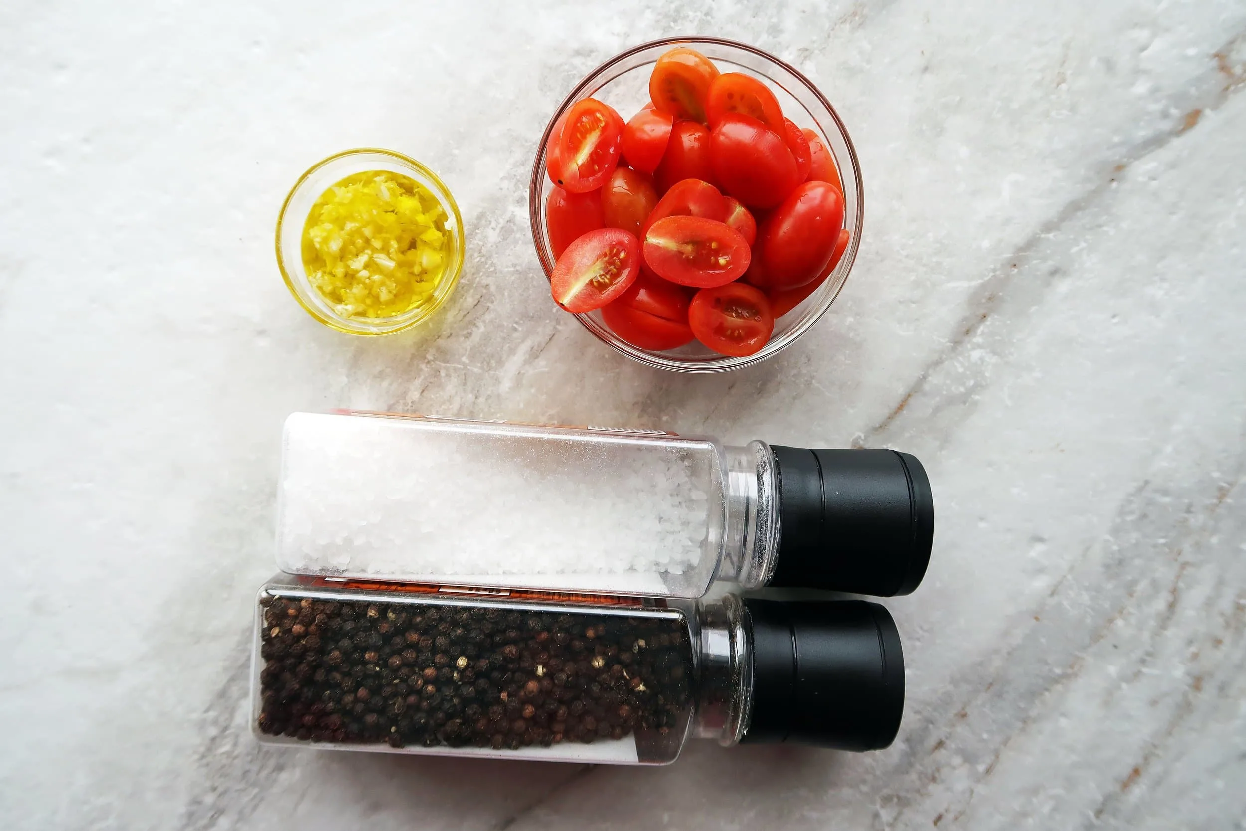 Bowls of cherry tomatoes, olive oil, and minced garlic with salt and pepper shakers.