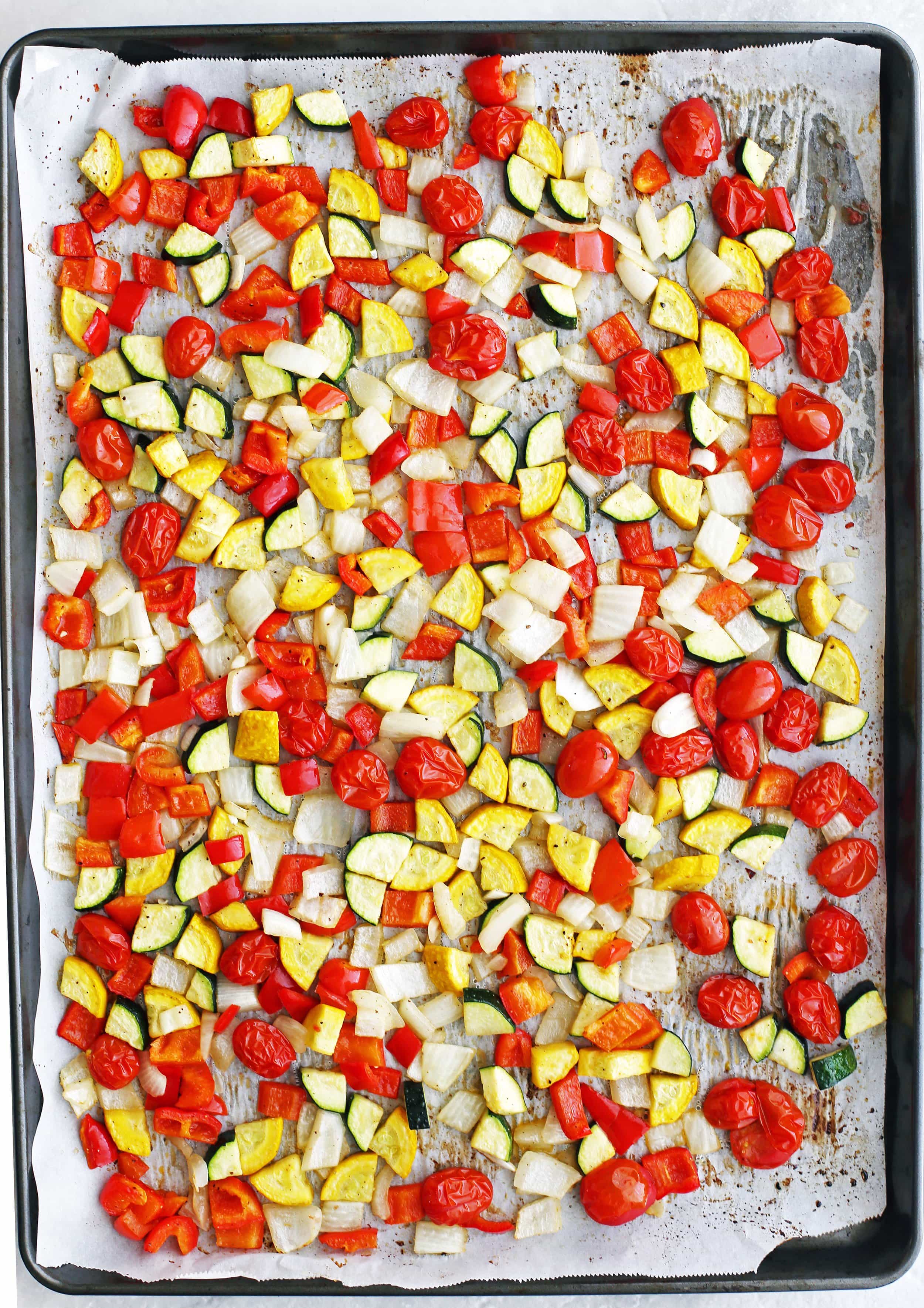 Roasted tomatoes, chopped zucchini, yellow squash, bell peppers, and onions on a baking sheet.