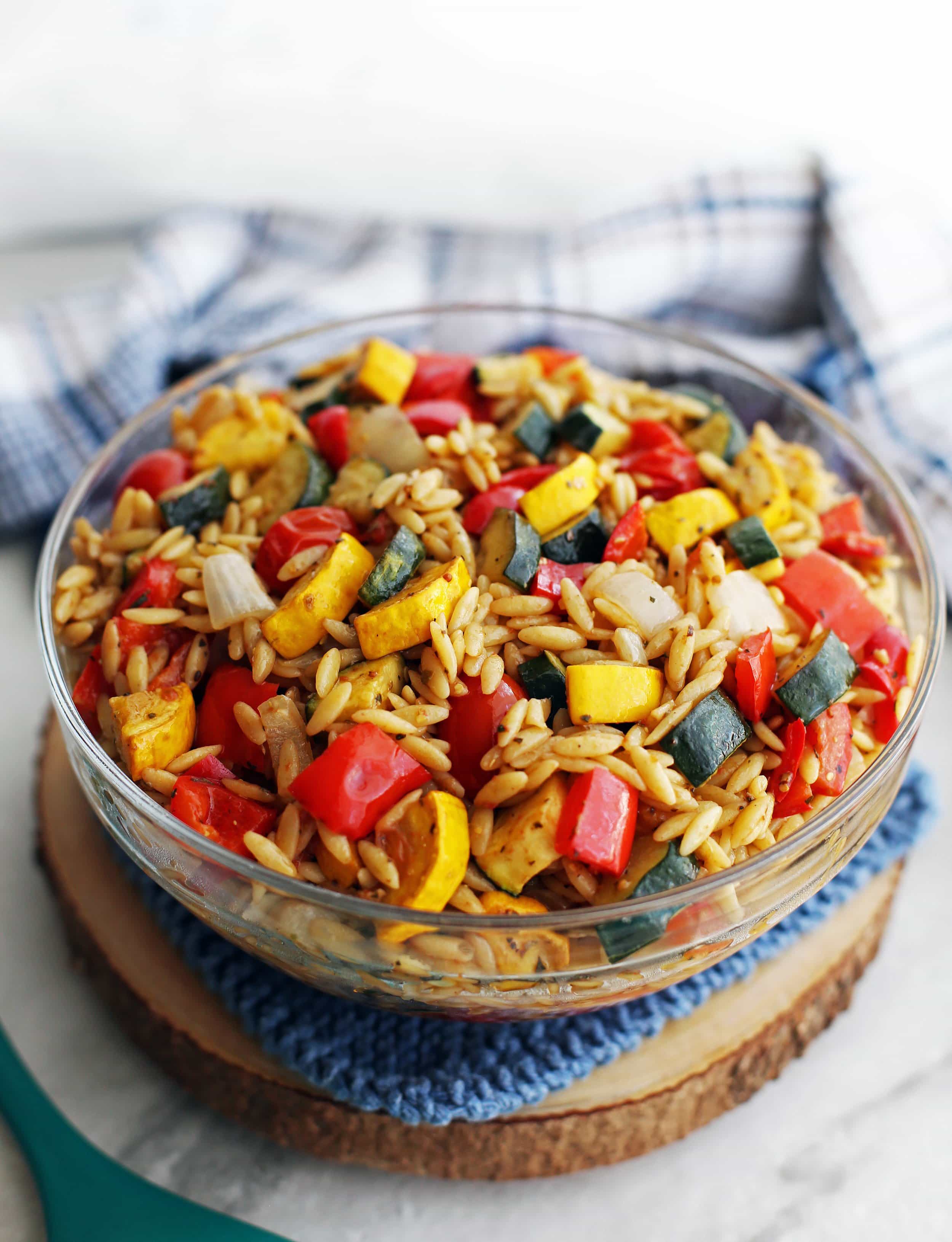 Roasted summer vegetable and orzo pasta salad with Dijon-balsamic vinaigrette in a large glass bowl.