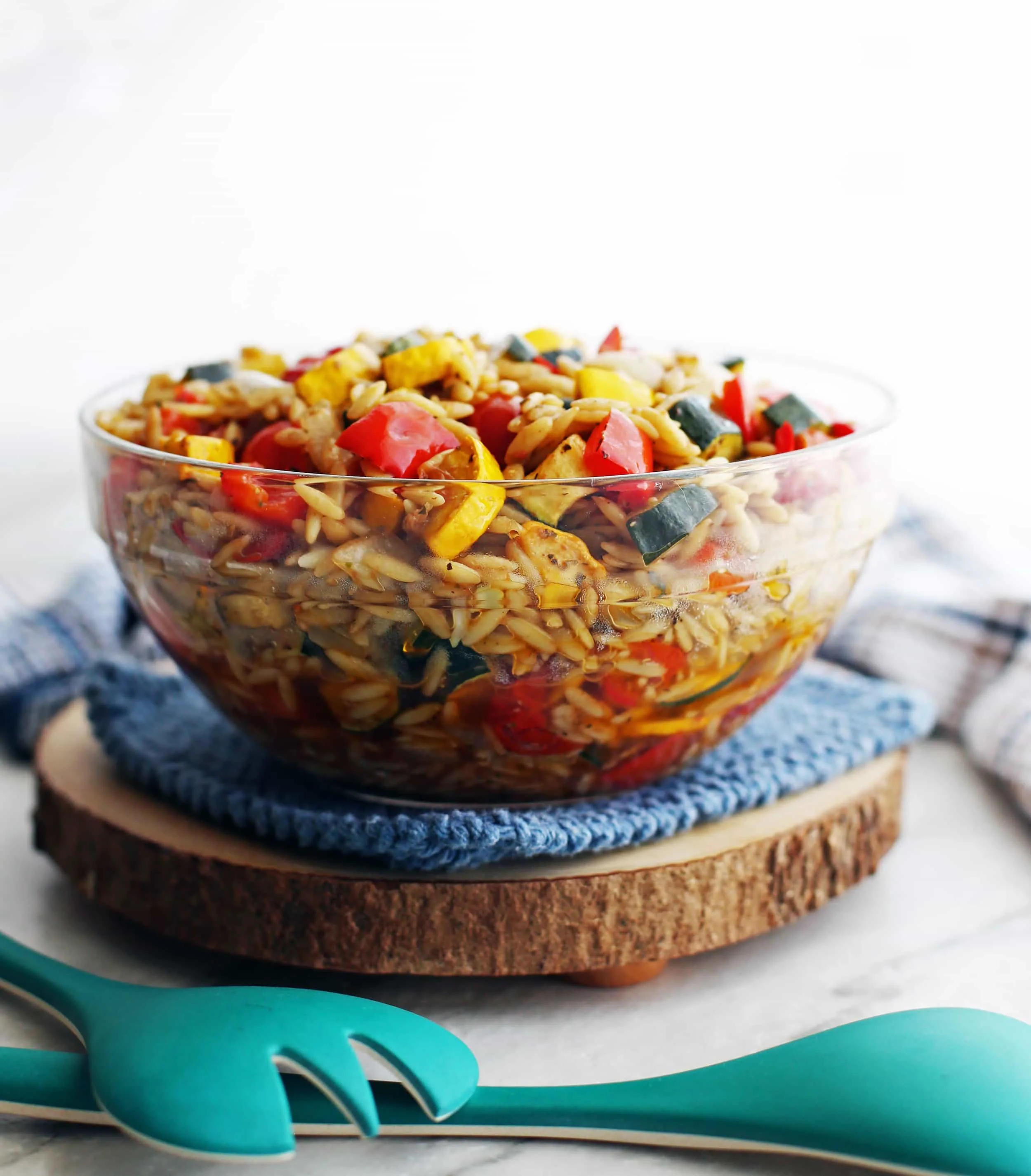 Roasted vegetables and orzo pasta tossed with a Dijon-balsamic dressing in a large glass bowl.