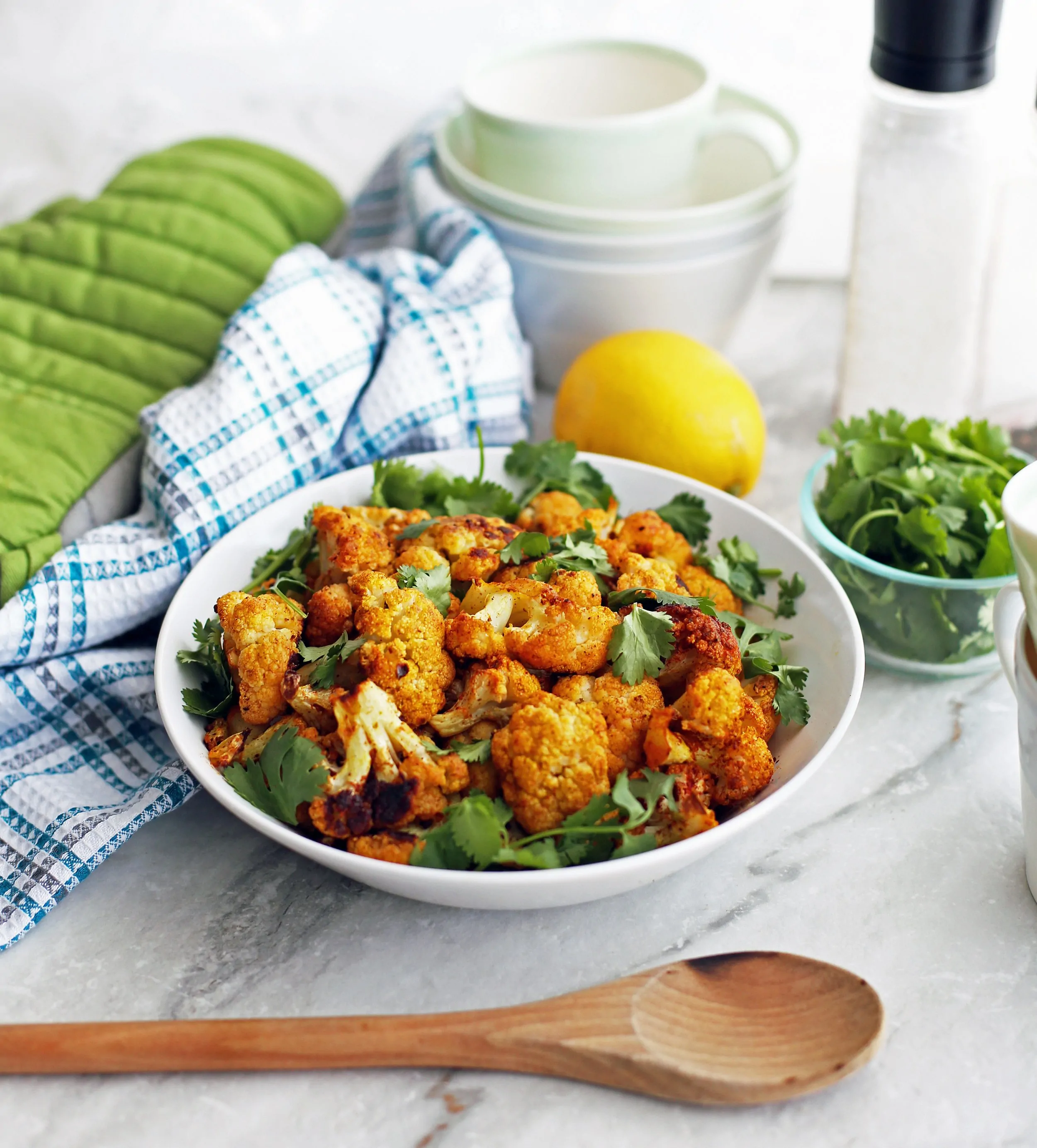 Side view of a wide bowl full of roasted spicy cauliflower with fresh cilantro.