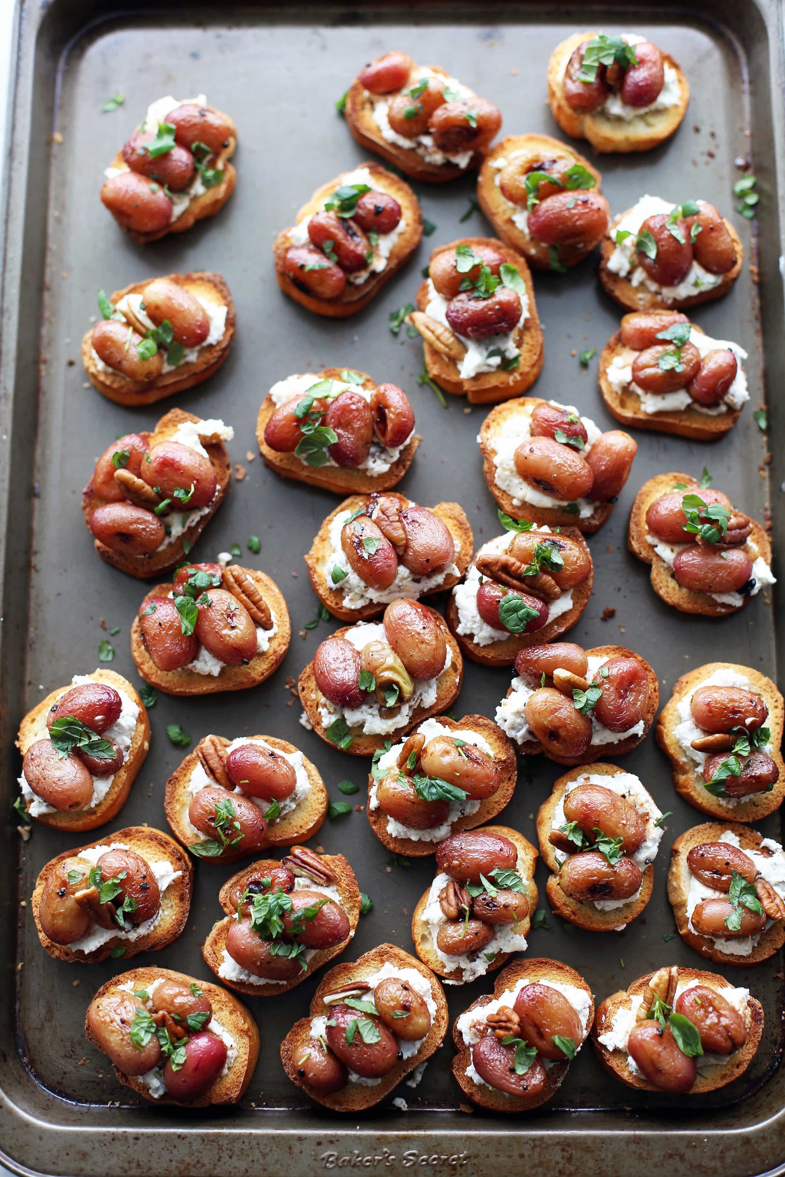 Overhead view of balsamic roasted grape and goat cheese crostini on a baking sheet.