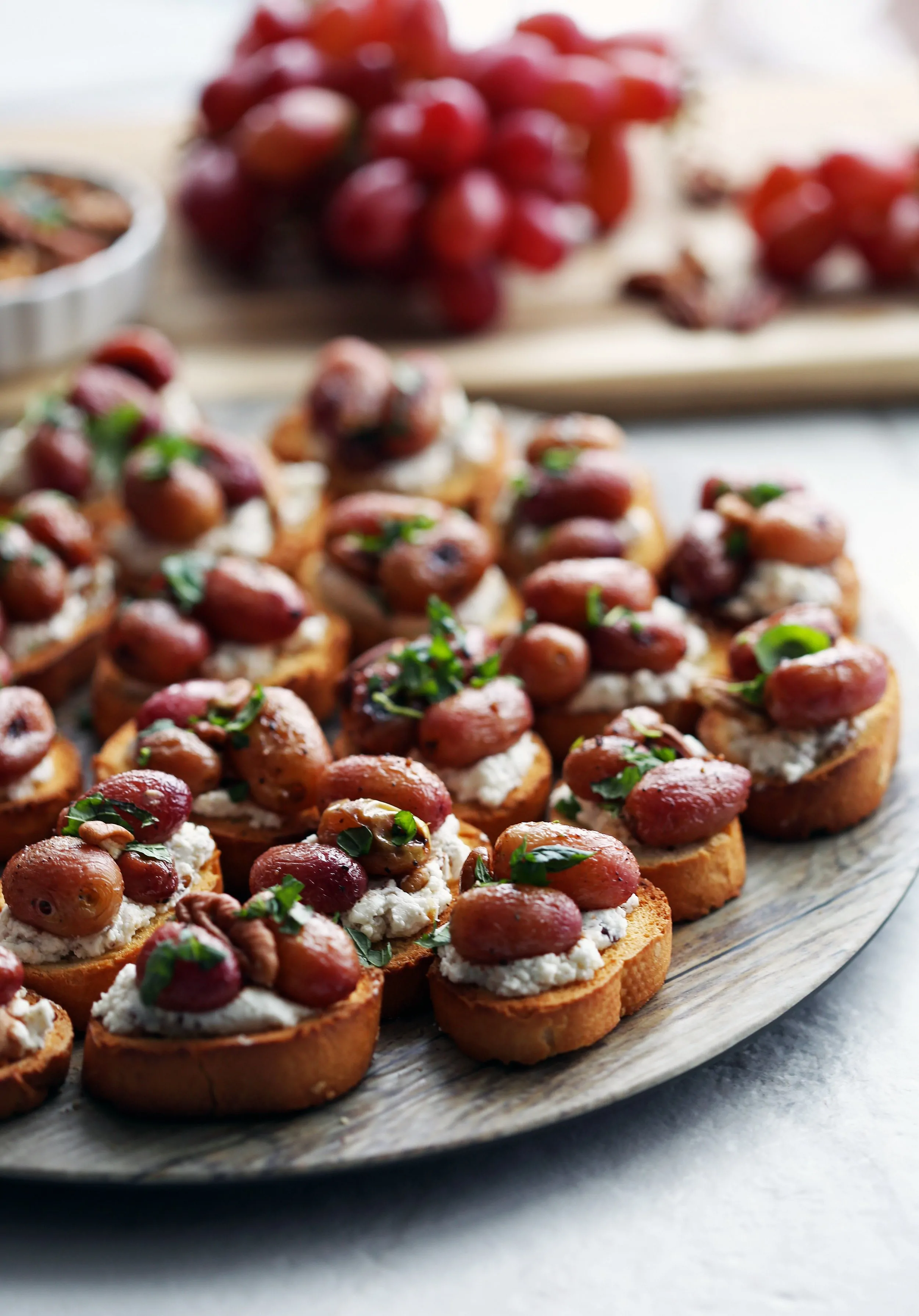 Side view of balsamic roasted grape and goat cheese crostini on a round platter.