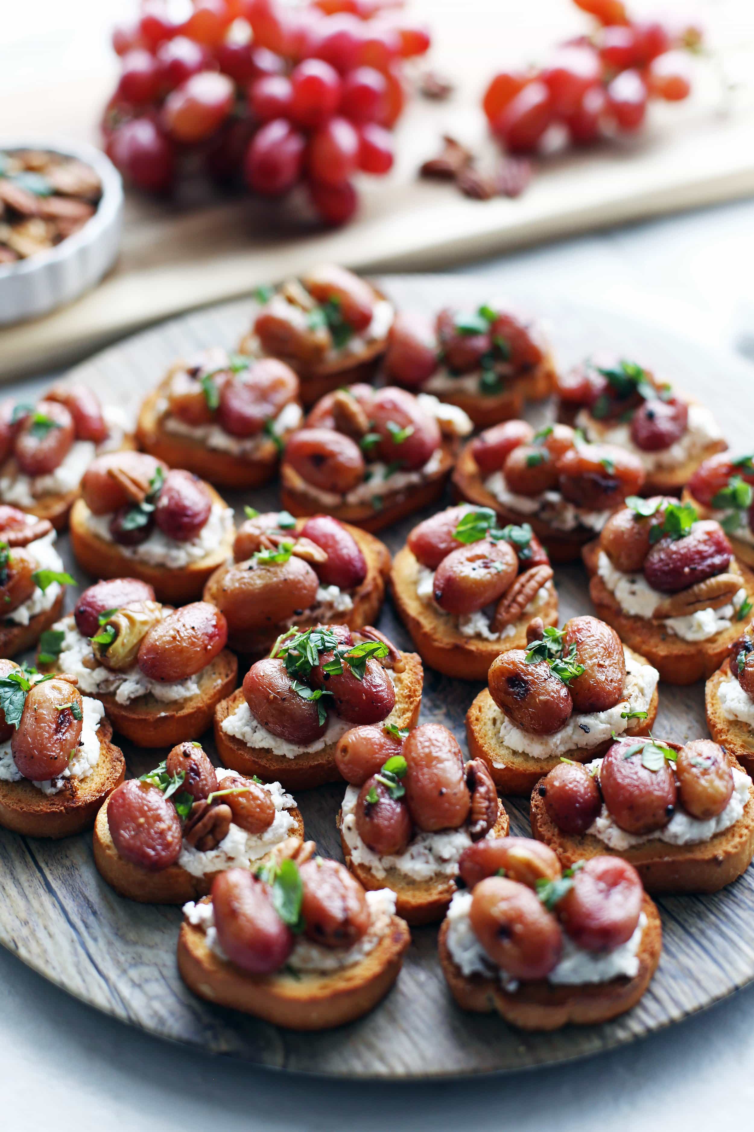 Balsamic roasted grape and goat cheese crostini, each garnished with mint and pecan pieces.