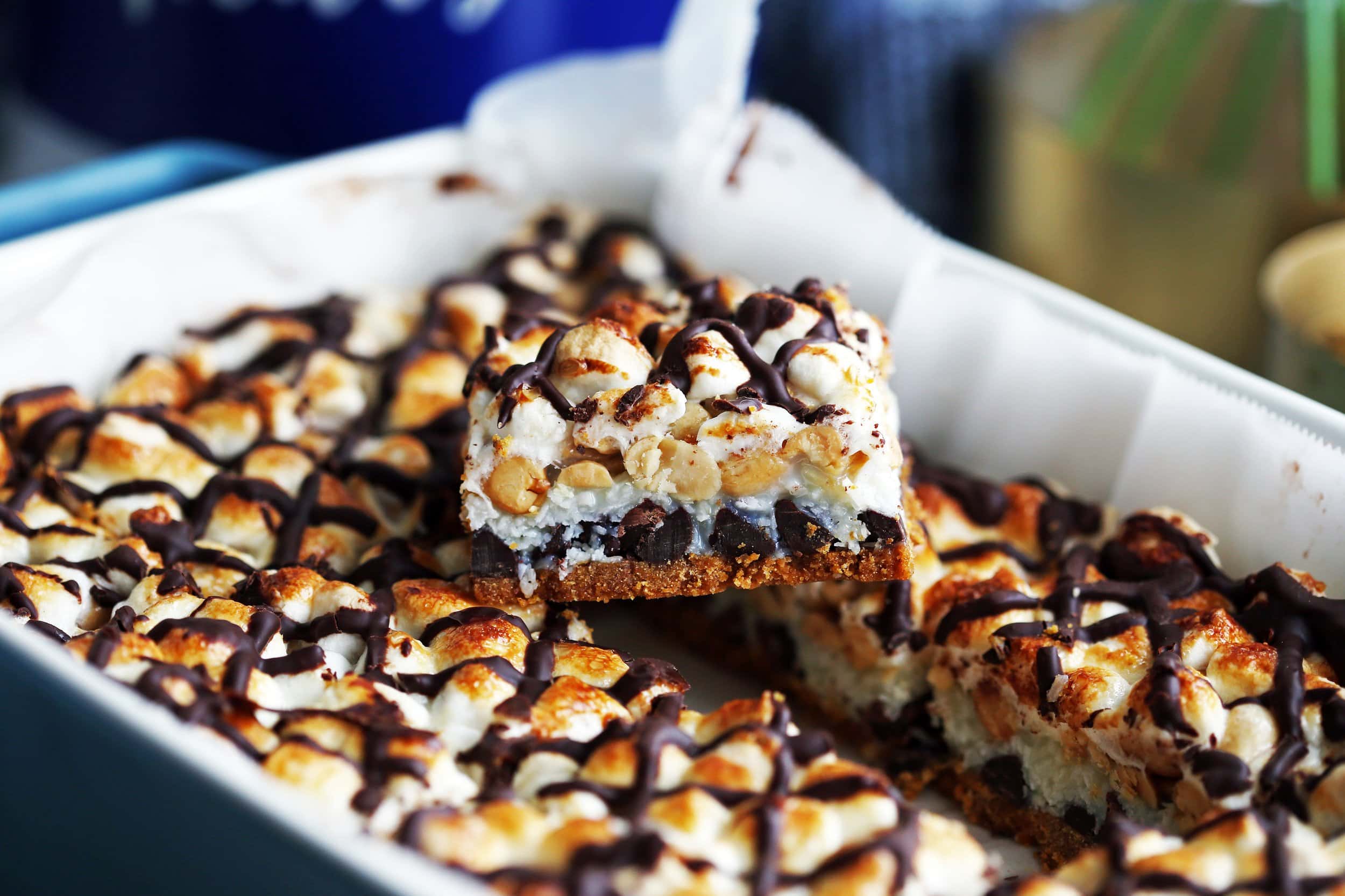 Side view of a baking dish filled with sliced seven layer rocky road magic bars with one bar sitting on top of the other bars.