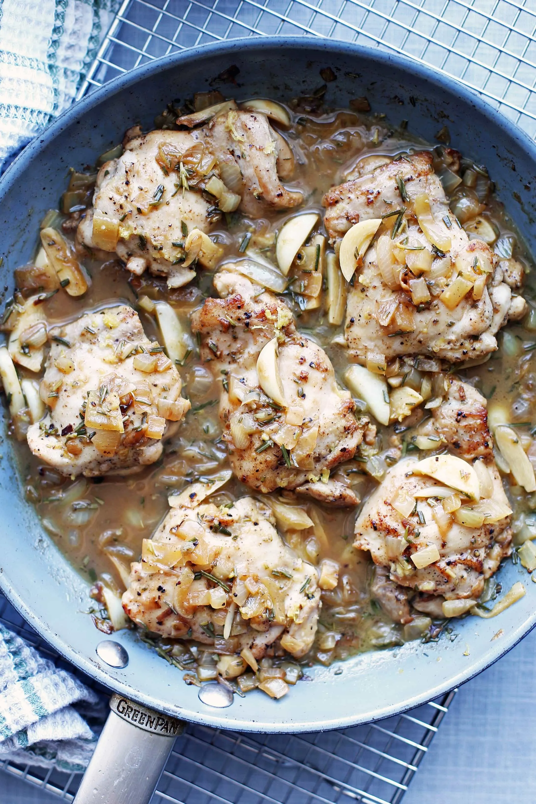 Six rosemary garlic chicken thighs covered with a garlic and chicken broth sauce in a large blue pan.