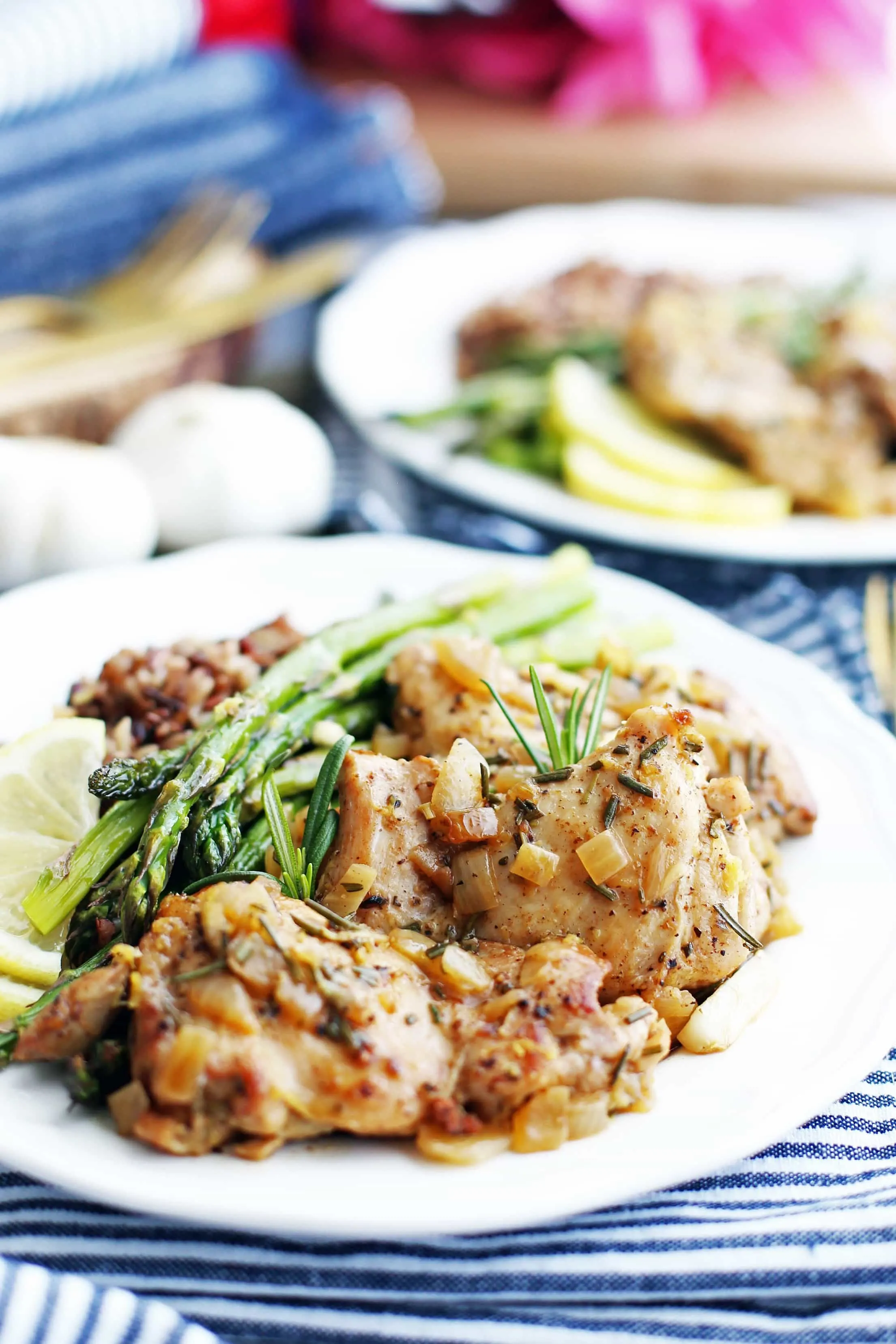 A closeup view of rosemary garlic chicken thighs on a white plate with asparagus and wild rice.